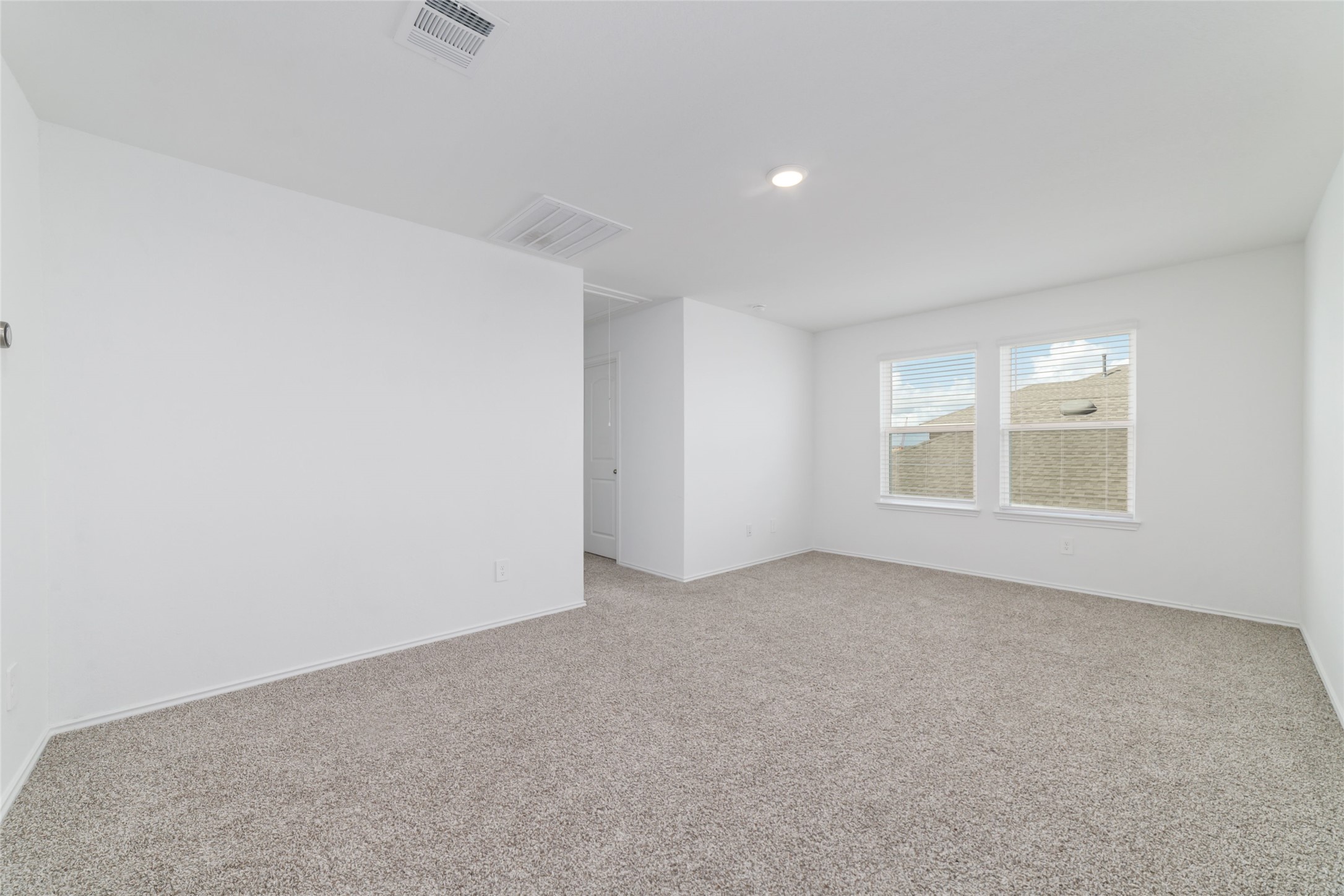 Located at the top of the stairs, this expansive and versatile upstairs game room offers a flexible bonus space ideal for a home theater, children's playroom, or casual secondary living area. The room features soft neutral carpeting, clean white walls, recessed lighting, and twin double windows that flood the open layout with abundant natural light while connecting seamlessly to the secondary bedrooms