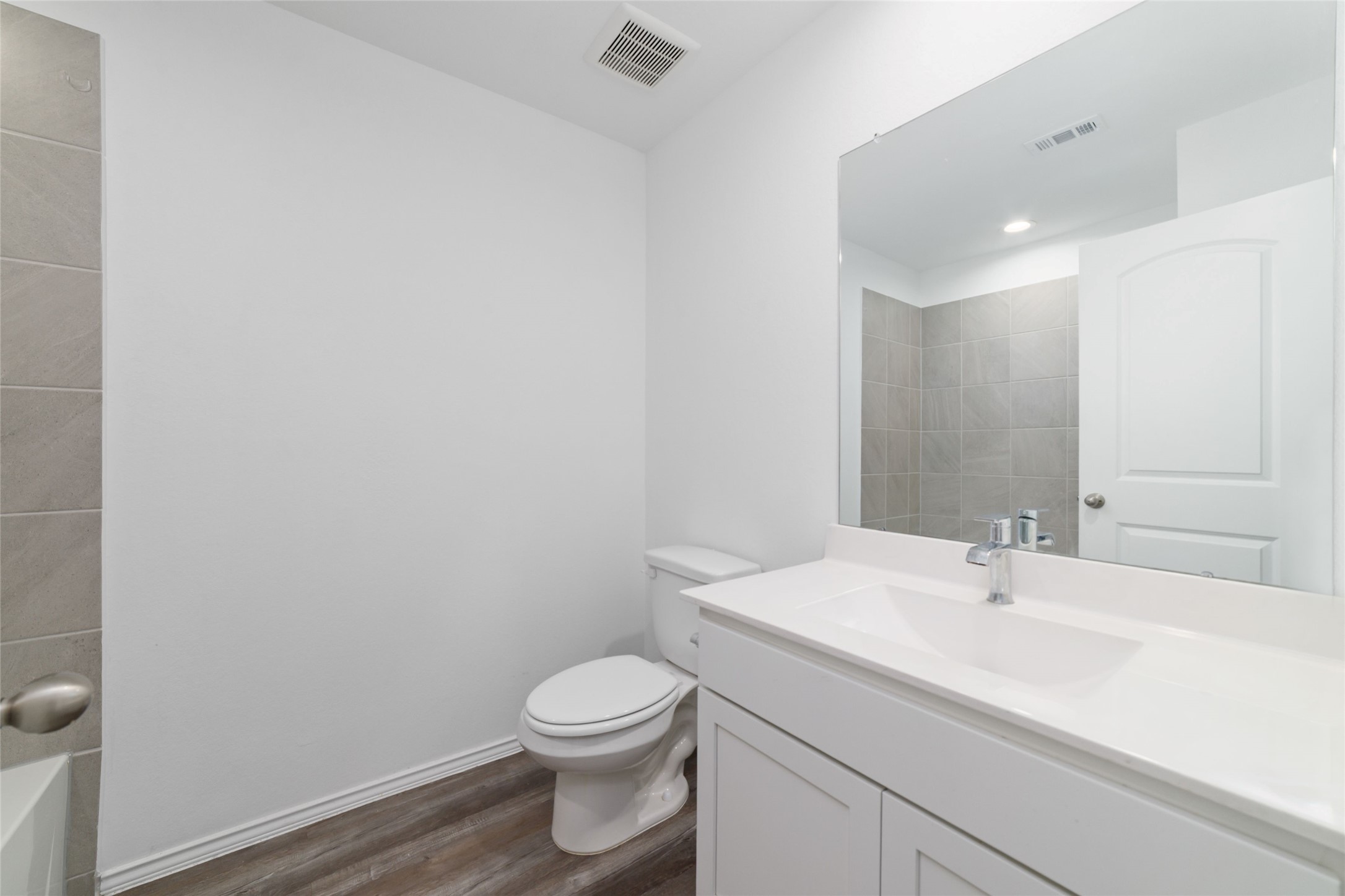 (Upstairs Full Bath): Crisp and spotless third full bathroom centrally positioned on the second floor to effortlessly service the game room and upstairs secondary bedrooms. This bright, move-in-ready space features dark wood-look flooring, a sleek white vanity with a seamless integrated sink, a large wall mirror, and a beautifully tiled shower/bathtub surround.