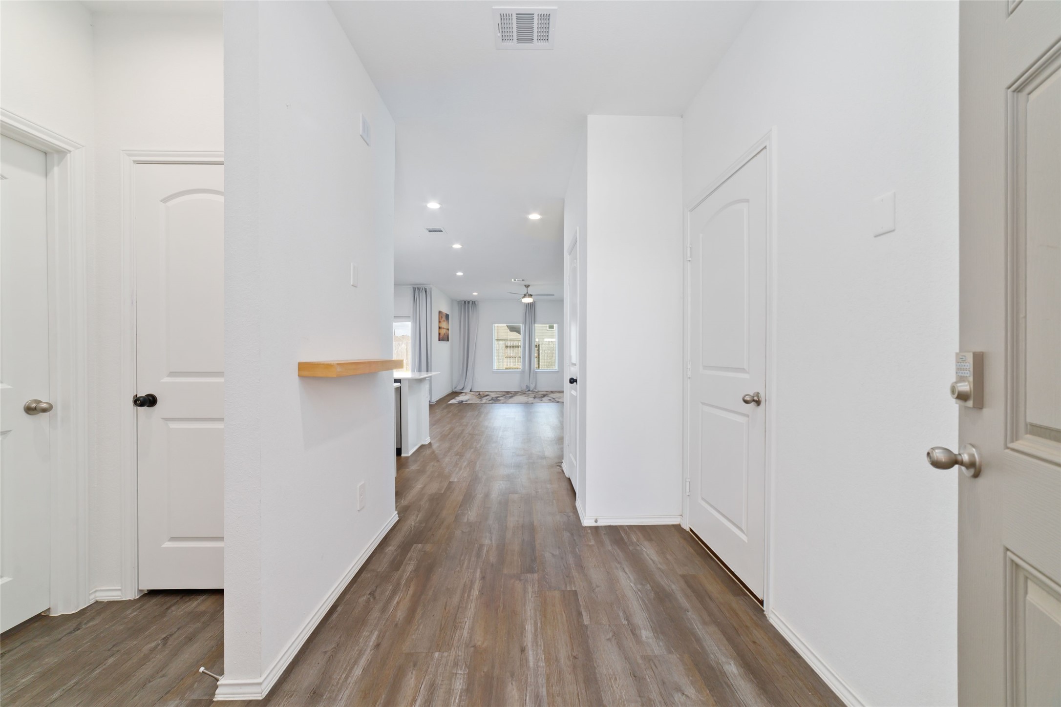 (Foyer & Main Hallway): A warm and welcoming front entryway featuring beautiful dark wood-look flooring, crisp white walls, and elegant brushed-nickel hardware. This thoughtfully designed central hallway provides seamless, private access to the downstairs secondary bedroom and bath while drawing the eye straight back into the open-concept living, dining, and entertaining spaces.