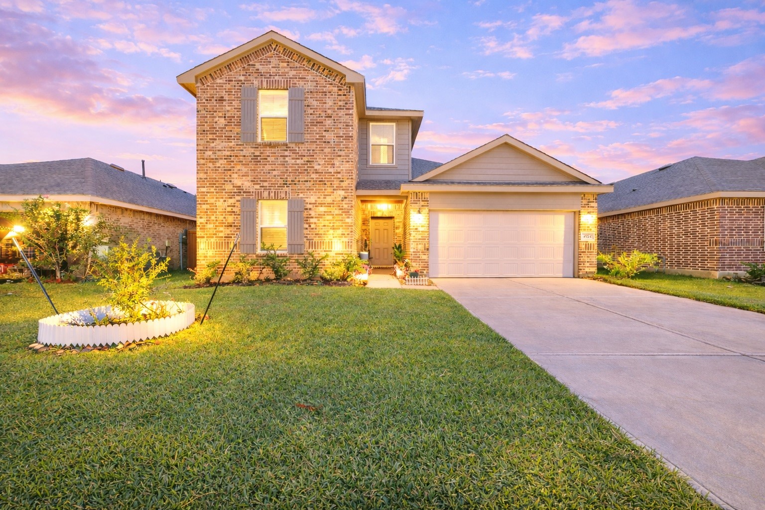 A captivating twilight exterior view of a two-story brick home, featuring a wide concrete driveway, and a pristine front lawn set against a vibrant dusk sky A captivating twilight exterior view of a two-story brick home, featuring a wide concrete driveway, and a pristine front lawn set against a vibrant dusk sky