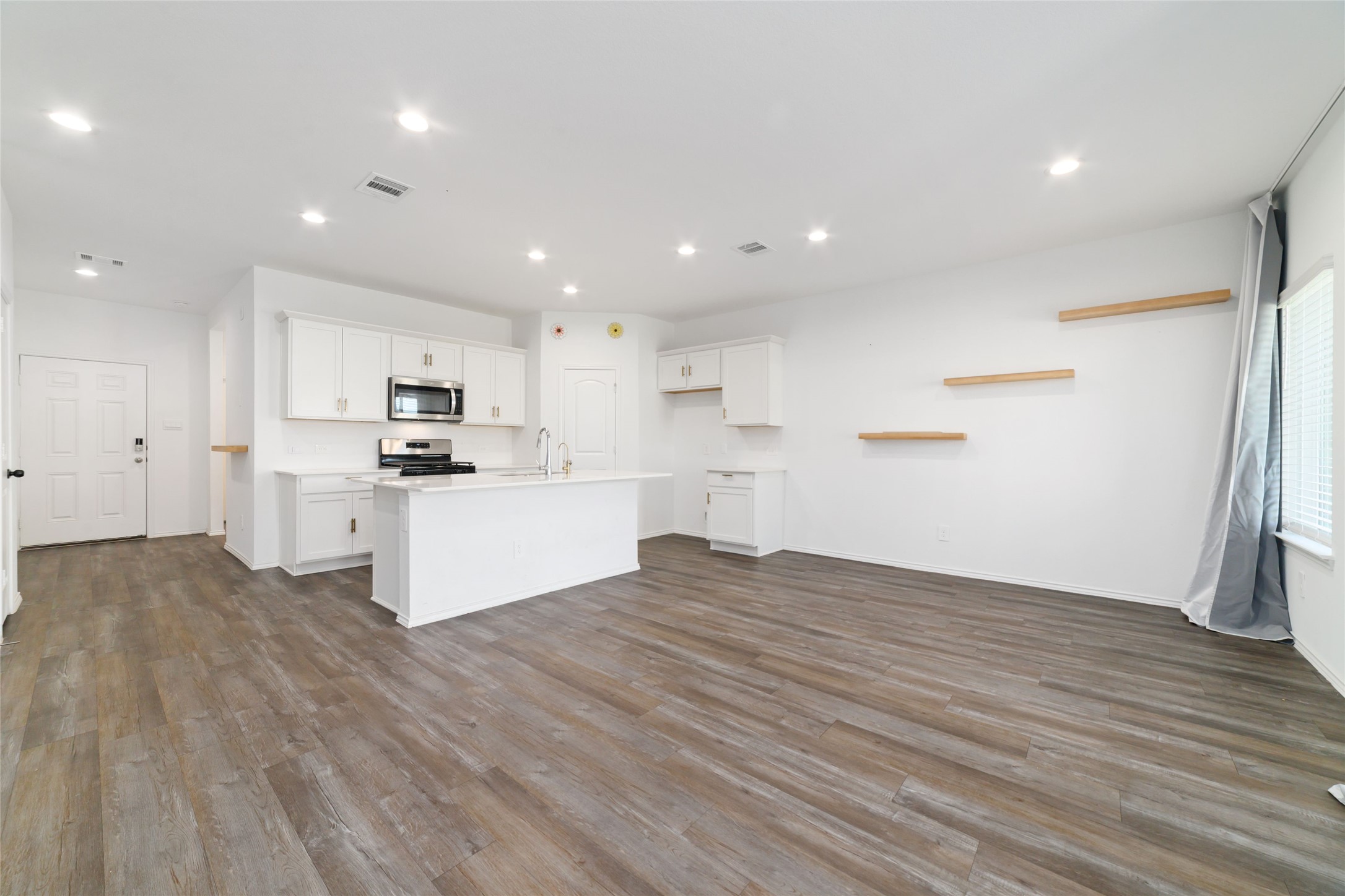 (Kitchen & Breakfast Area): The heart of the home features a seamless open-concept design where the gourmet kitchen flows effortlessly into the bright dining and breakfast area. Highlighted by rich wood-look flooring, a large center entertaining island with seating overhang, abundant cabinetry, and custom floating wall shelves, this versatile space offers plenty of room for a full dining table right next to the natural light of the backyard window.