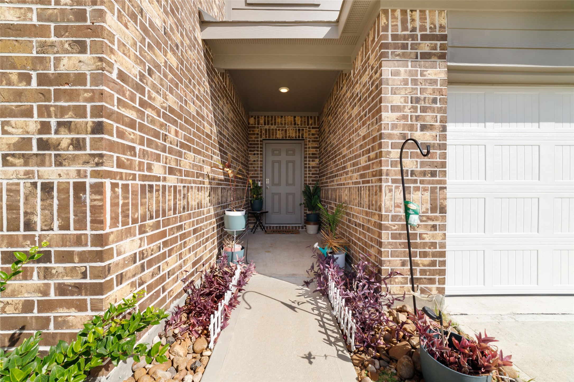 Focused close-up of the front entryway and porch alcove, featuring a modern grey front door set within brick walls with small potted plants, a welcome mat, and decorative accents Focused close-up of the front entryway and porch alcove, featuring a modern grey front door set within brick walls with small potted plants, a welcome mat, and decorative accents