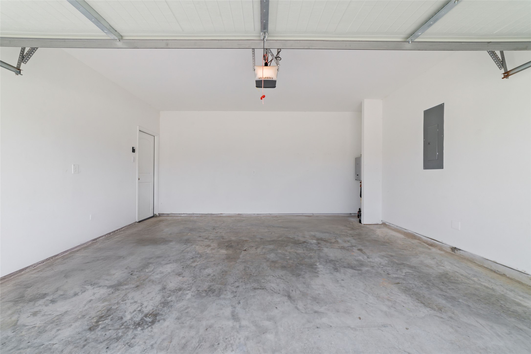 Inside view of a clean, empty attached two-car garage with white walls, a durable concrete floor, and an overhead automated door opener mechanism