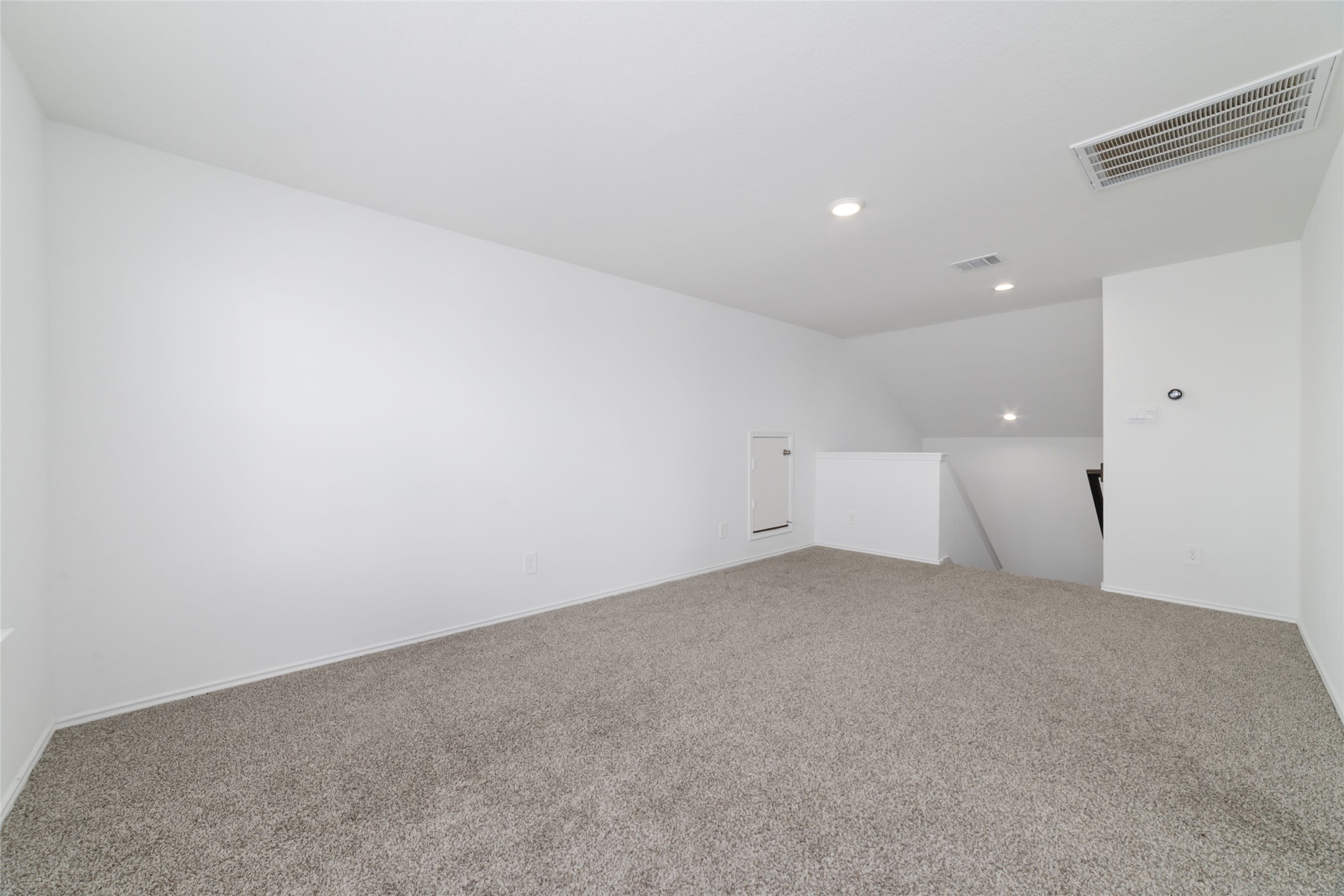 Located at the top of the stairs, this expansive and versatile upstairs game room offers a flexible bonus space ideal for a home theater, children's playroom, or casual secondary living area. The room features soft neutral carpeting, clean white walls, recessed lighting, and twin double windows that flood the open layout with abundant natural light while connecting seamlessly to the secondary bedrooms