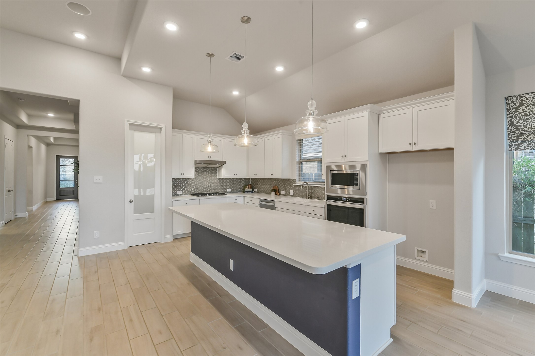 This gorgeous kitchen includes custom lighting, stainless steel appliances, gas oven and stove, designer backsplash, a large walk in pantry, an island, and generous cabinetry.