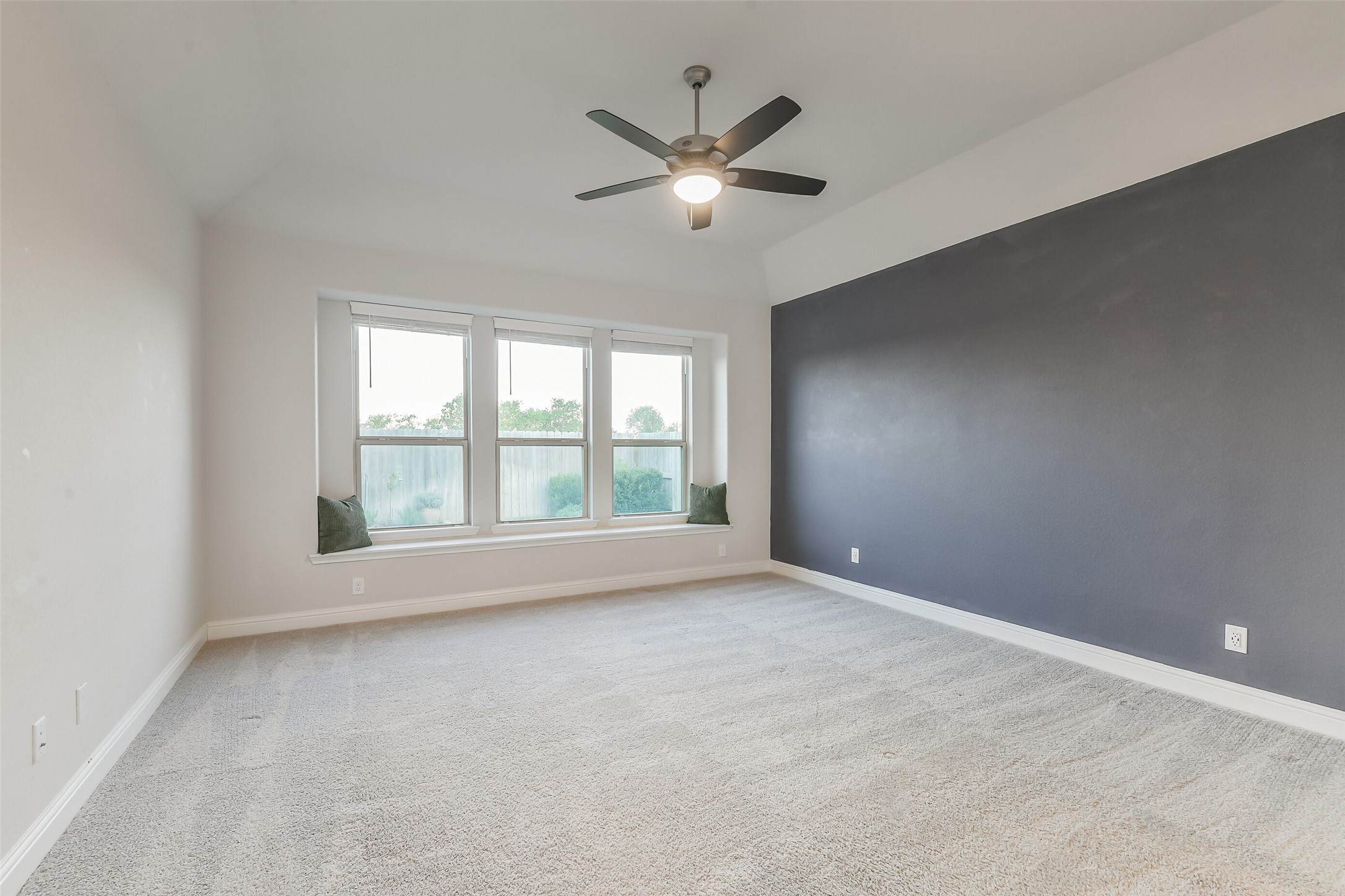 The primary bedroom features window seating, a ceiling fan, beautiful accent wall, and plenty of natural light from the windows with blinds for privacy.