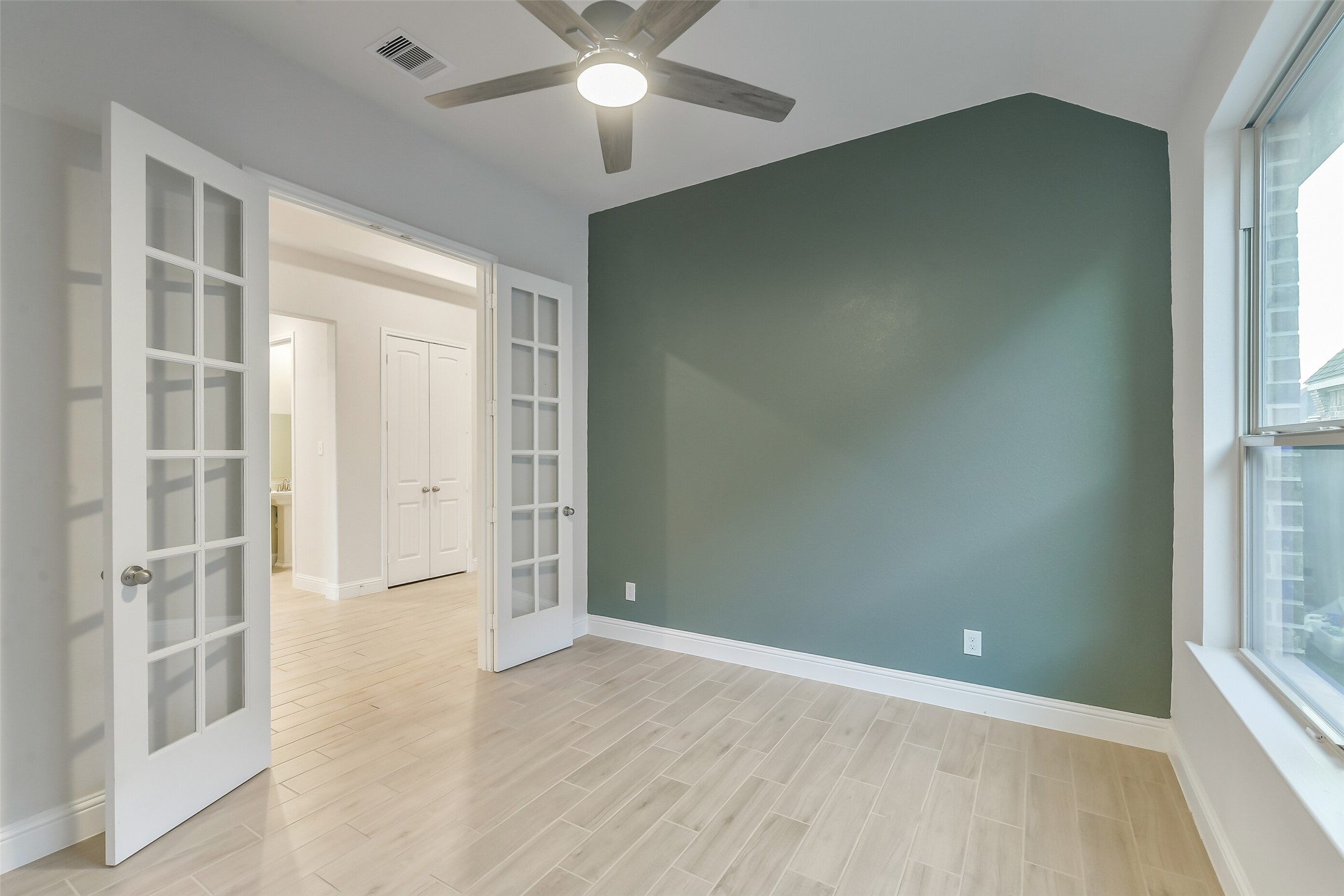 This home office or extra room features a gorgeous accent wall, ceiling fan, and glass paned French doors.
