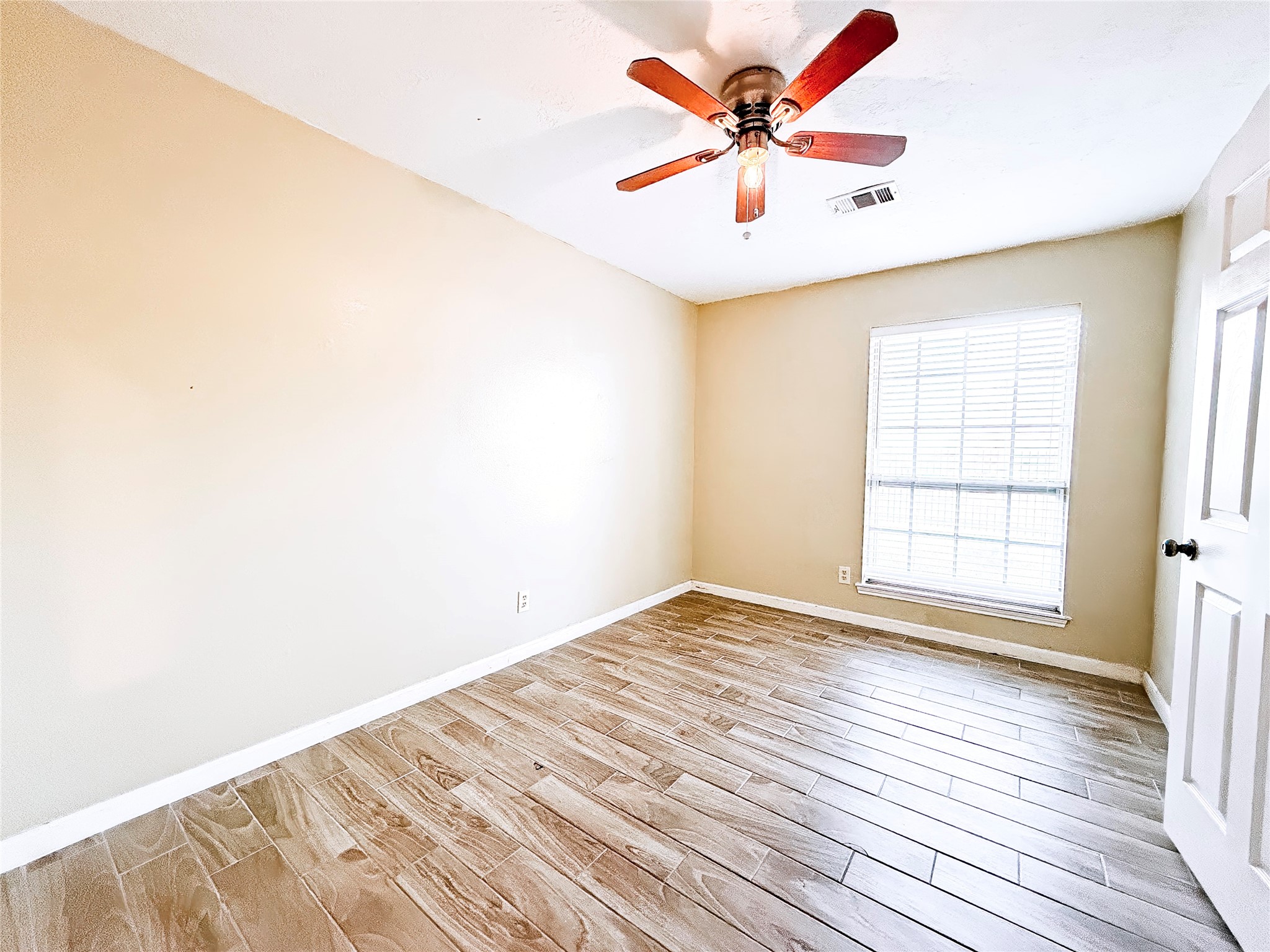 Bright and inviting room featuring wood-look tile flooring, a ceiling fan, and a large window that allows natural light to fill the space.