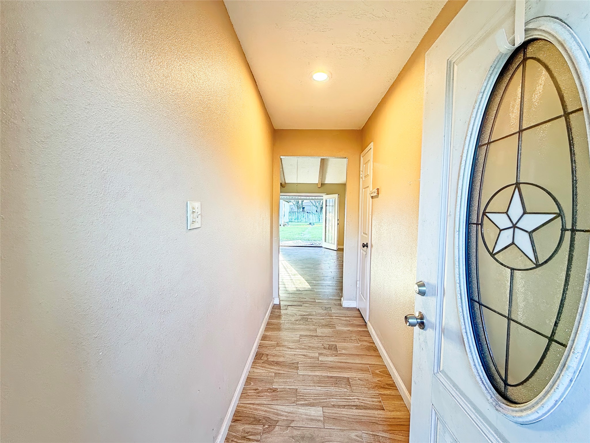 Inviting entryway with wood-style flooring leads to a bright living space and a view of the backyard, highlighted by a distinctive star-patterned glass door.