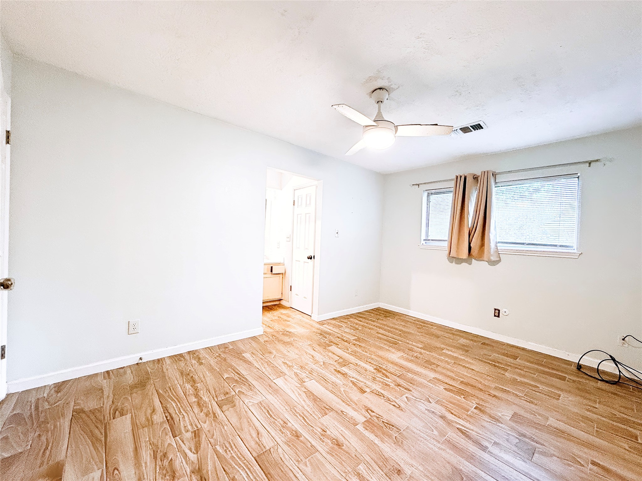 Bright and spacious bedroom featuring wood-style flooring, a ceiling fan, and a convenient en-suite bathroom.