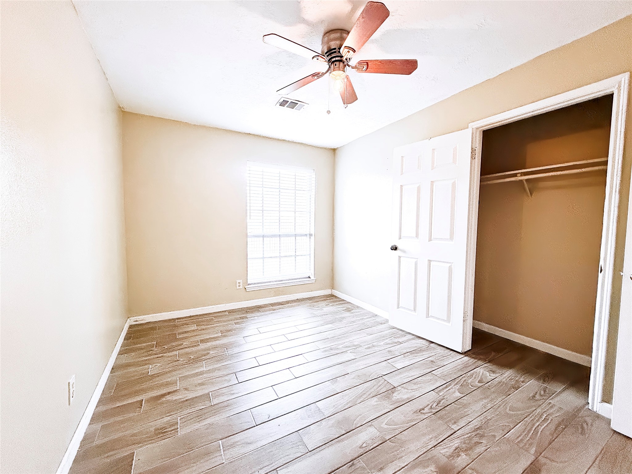 Bright and inviting bedroom featuring wood-look tile flooring, a ceiling fan, and ample natural light from a large window, complete with a spacious closet.