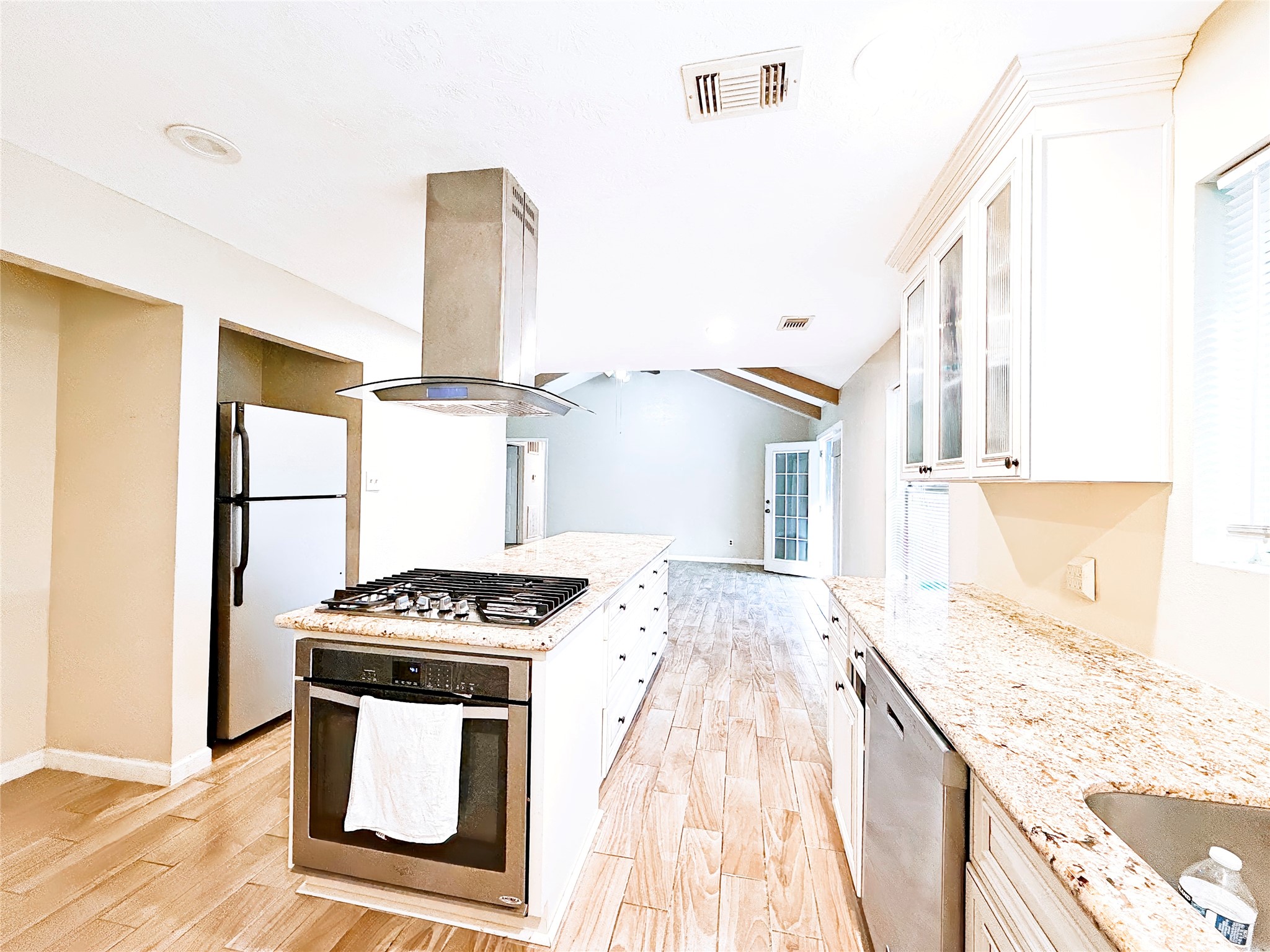 A spacious kitchen featuring modern stainless steel appliances, a sleek range hood, and granite countertops, complemented by ample natural light and elegant cabinetry.