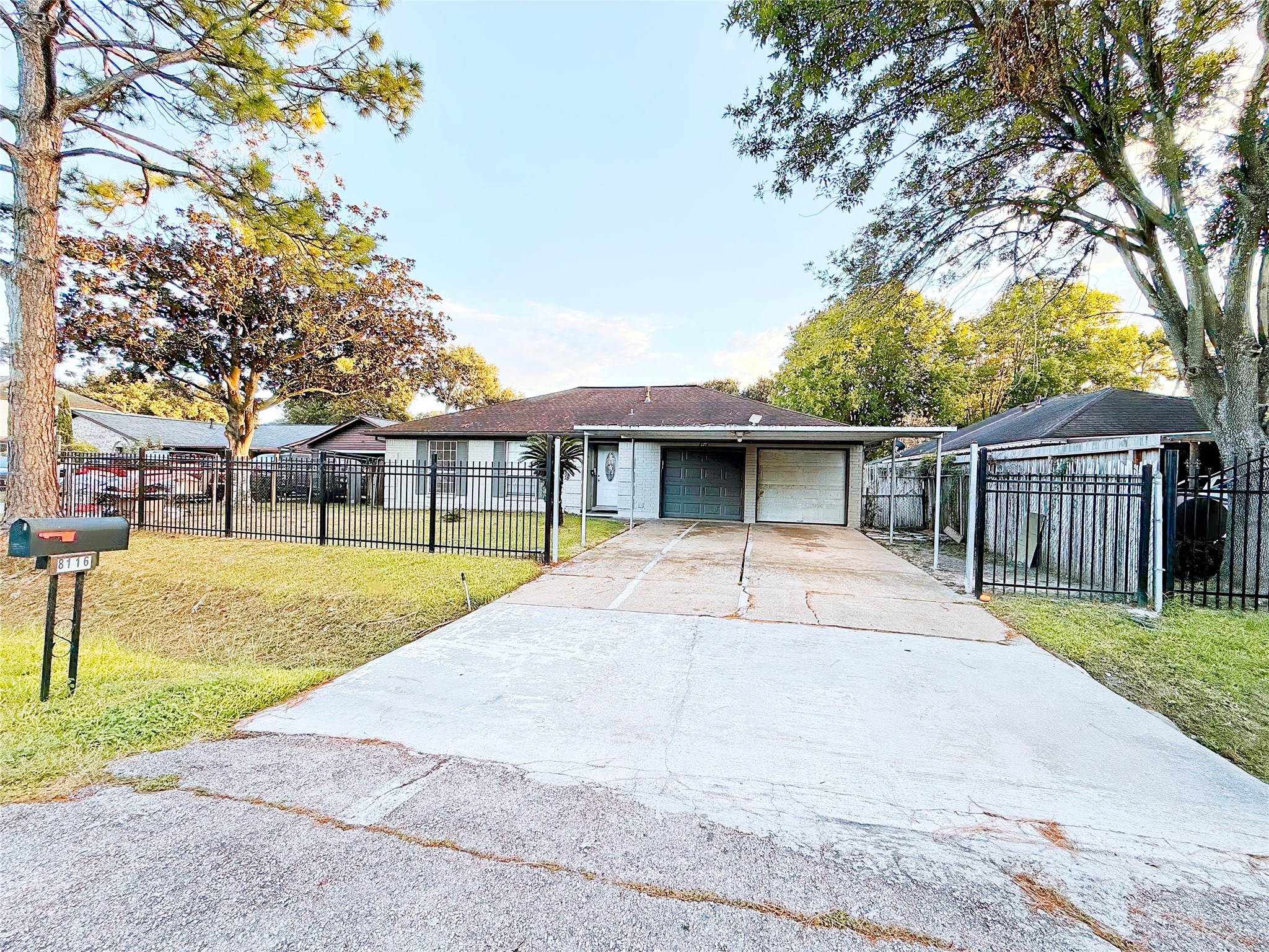 Charming ranch-style home with a spacious driveway and a secure, gated front yard. Surrounded by mature trees, it offers a serene and private setting.
