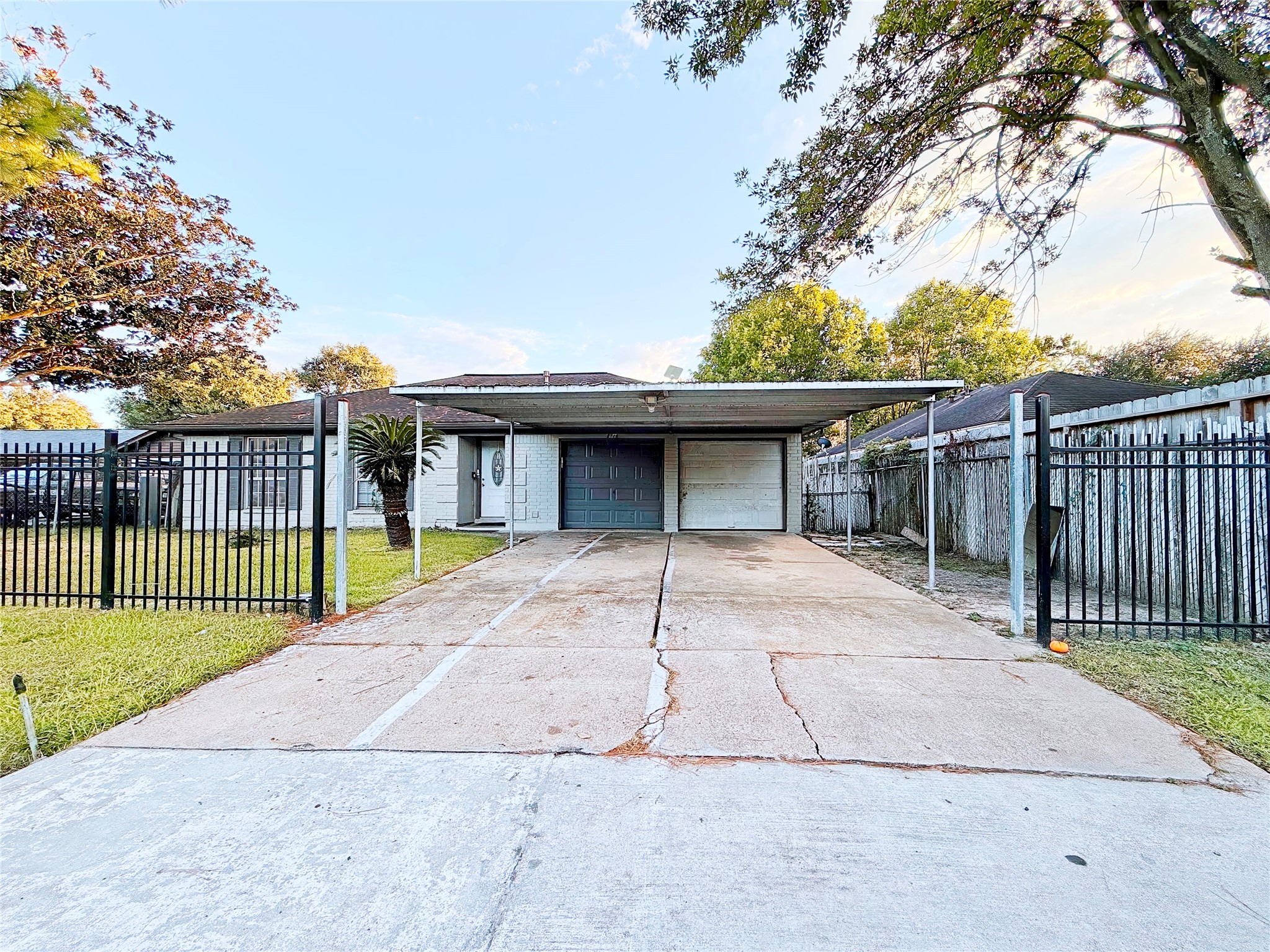 Charming home with a spacious driveway and a secure gated entrance, featuring a two-car carport and lush greenery surrounding the property for added privacy.