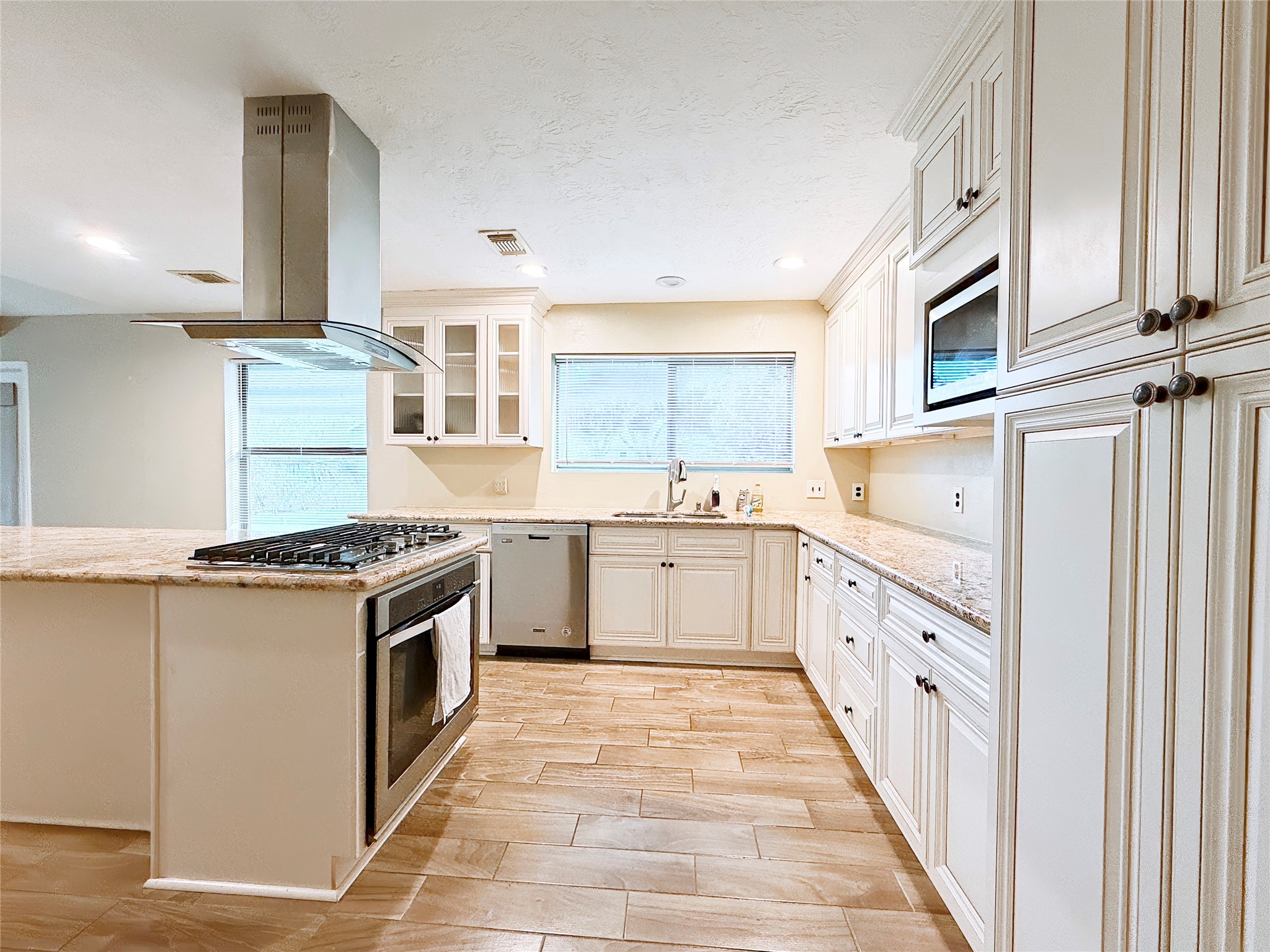 Spacious kitchen featuring elegant white cabinetry, granite countertops, and a modern stainless steel stove with a sleek range hood, complemented by ample natural light and tiled flooring.