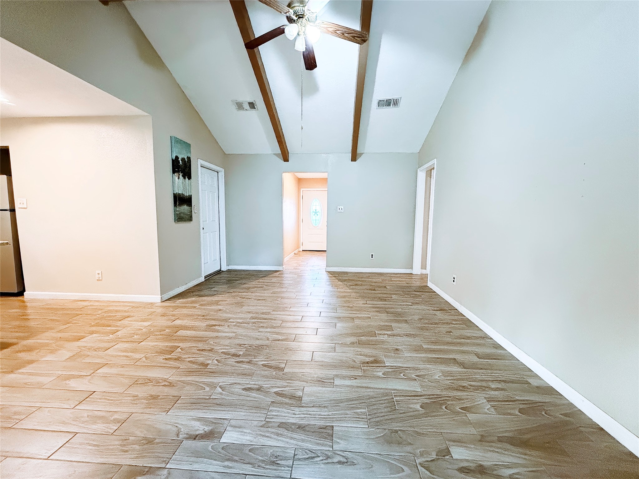 Spacious living area with high vaulted ceilings, exposed wooden beams, and elegant wood-look tile flooring, offering a warm and inviting atmosphere.