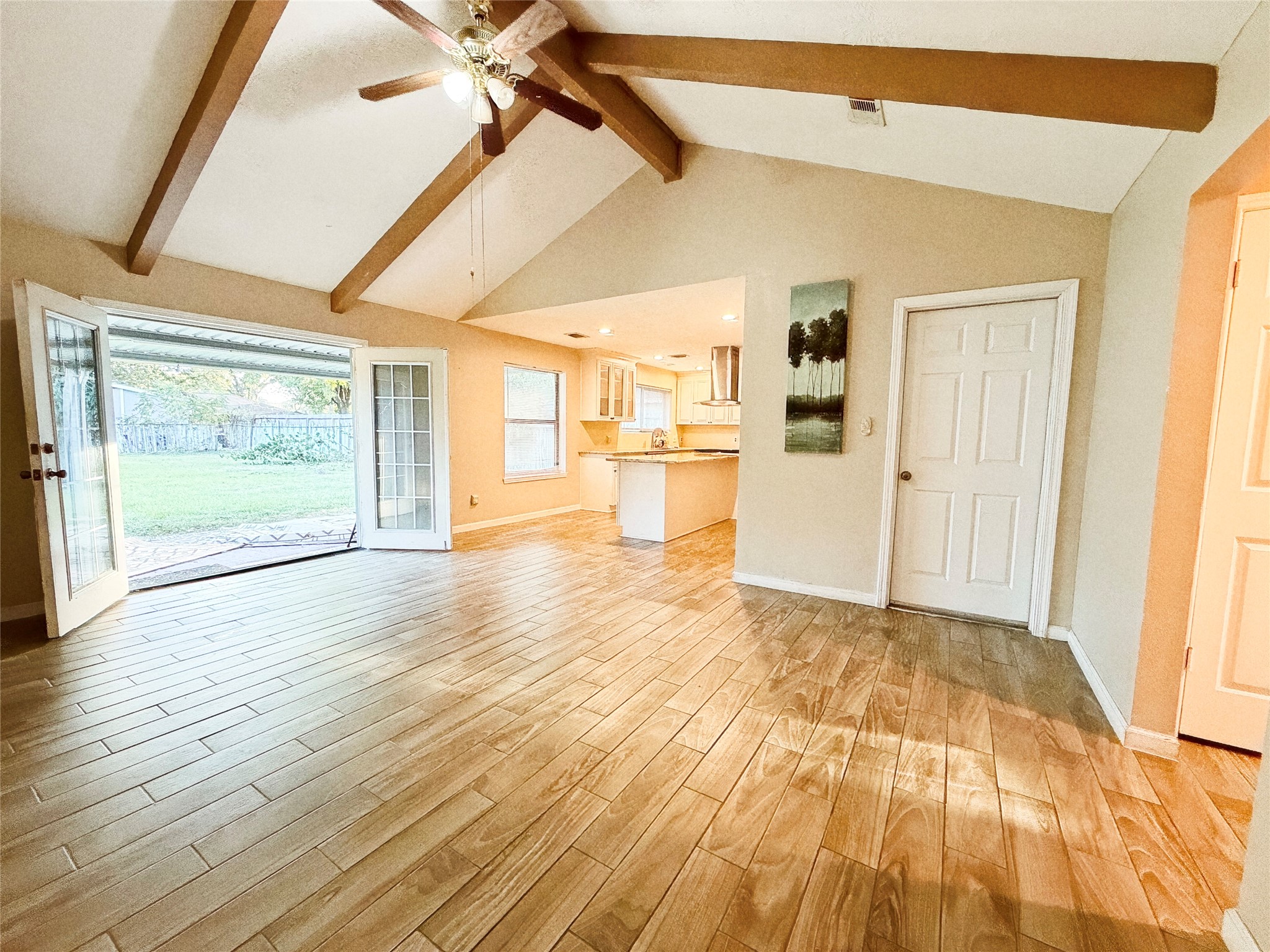 Spacious living area with vaulted ceilings and exposed beams, featuring elegant wood-look tile flooring and French doors leading to a serene backyard.