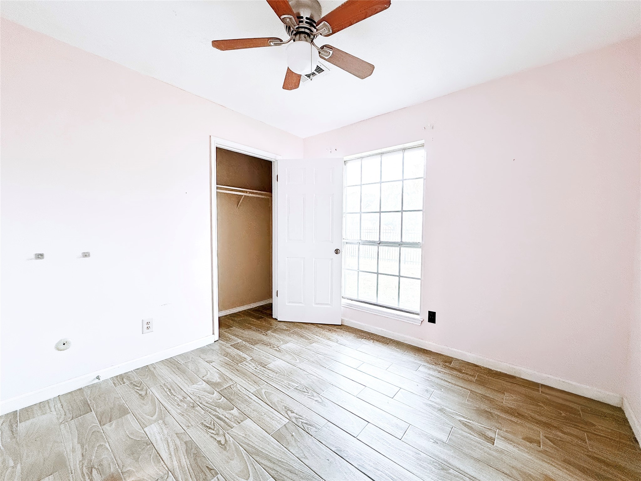 Bright and airy room featuring wood-look tile flooring, a ceiling fan, and a large window for natural light.