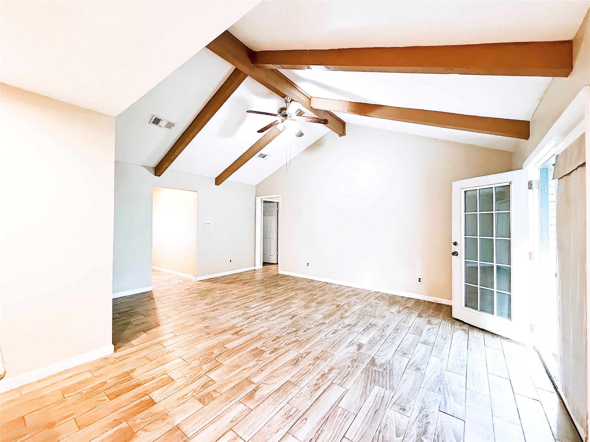 Spacious living area with high vaulted ceilings and exposed wooden beams, featuring elegant wood-look tile flooring and abundant natural light from French doors.