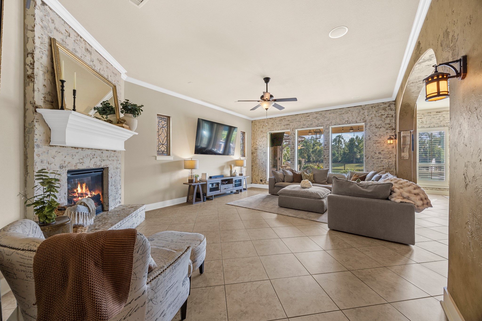 Beautifully appointed family room featuring a whitewashed brick fireplace, decorative accent walls, crown molding, and large windows overlooking the backyard.