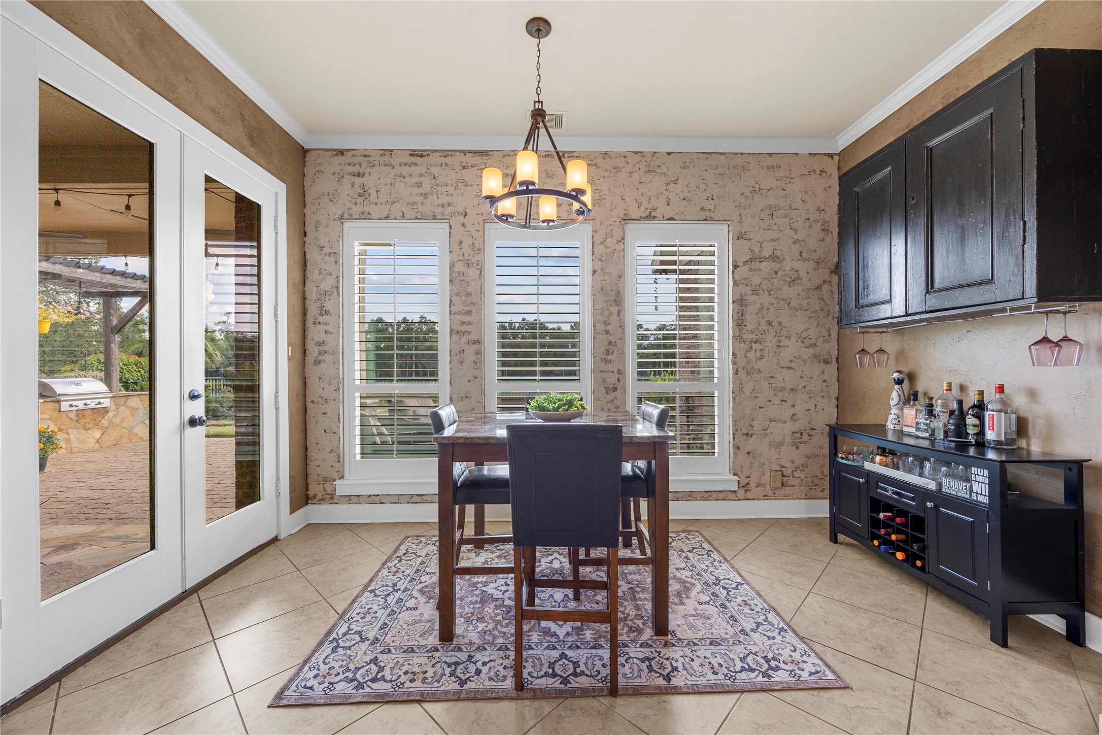 Charming breakfast area featuring decorative brick accents, plantation shutters, statement lighting, and French doors leading to the outdoor living space.