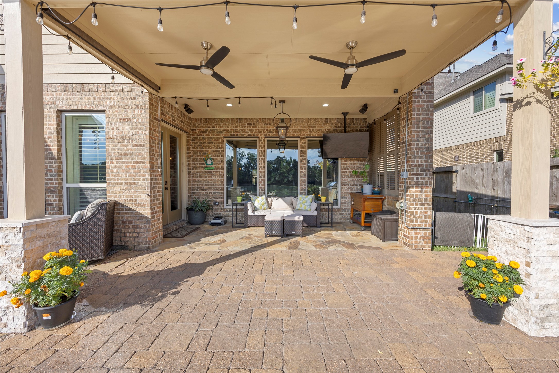 Spacious covered patio featuring dual ceiling fans, string lighting, recessed lighting, and a comfortable seating area for year-round enjoyment.