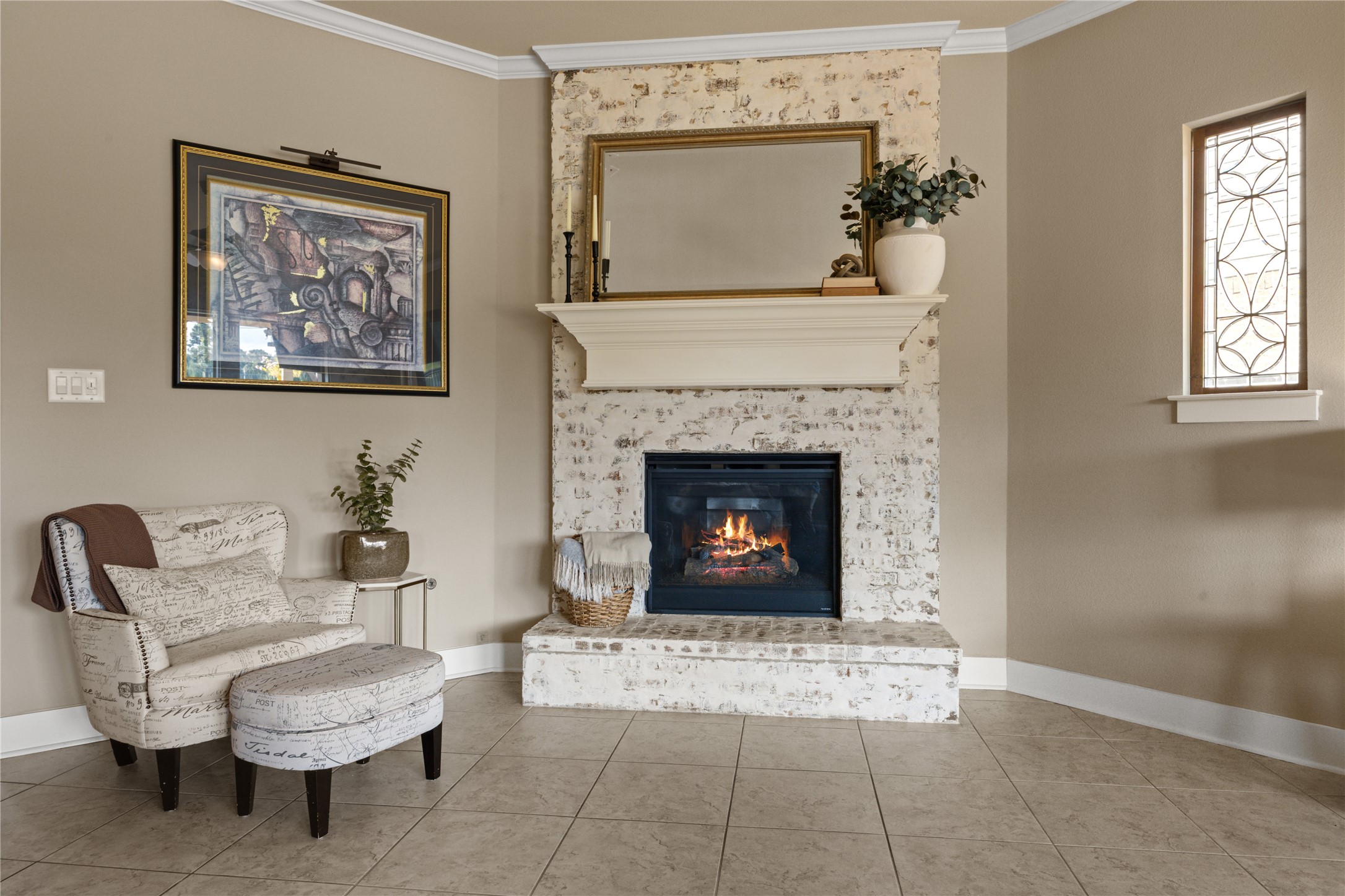 The stunning whitewashed brick fireplace serves as a focal point, complemented by a classic white mantel and decorative accent window.