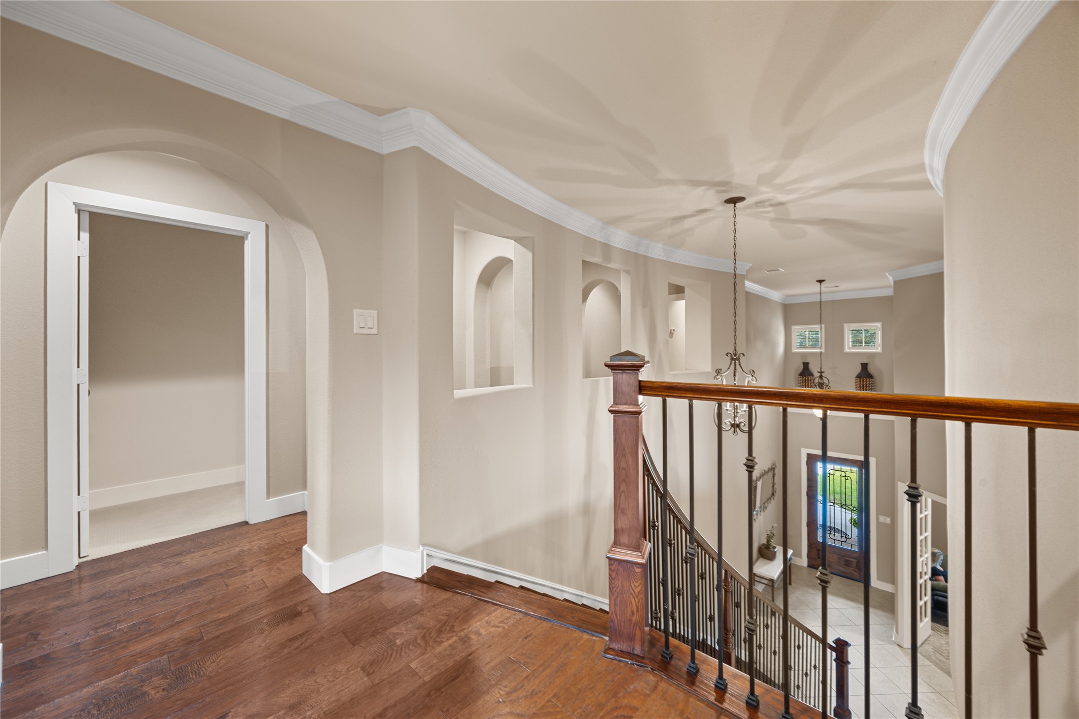 Elegant upstairs landing featuring beautiful wood flooring, architectural archways, decorative crown molding, and an open railing overlooking the lower level.