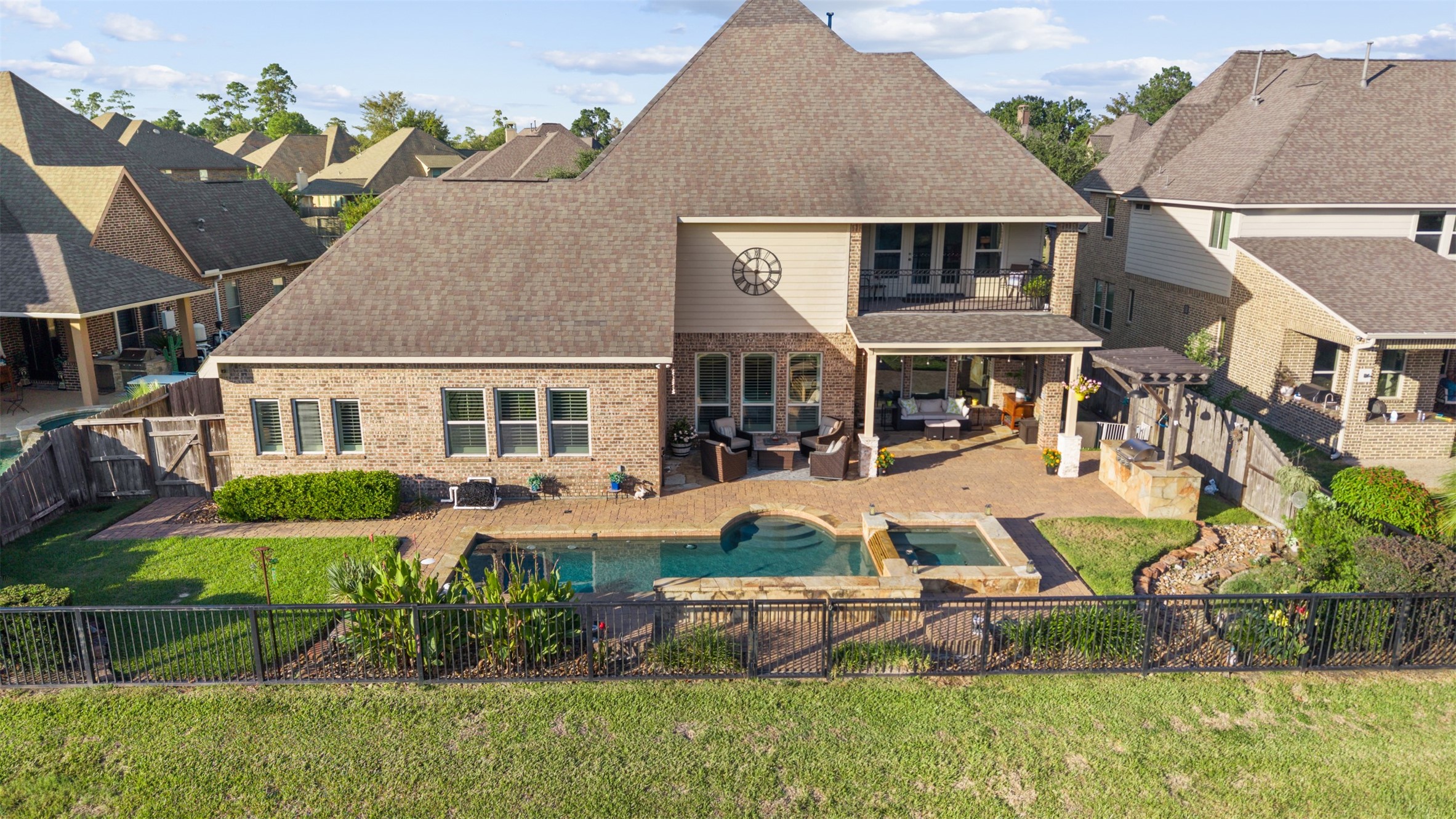 Elevated rear view highlighting the home's impressive architecture, second-story balcony, covered patio, outdoor kitchen, pool, and spa.