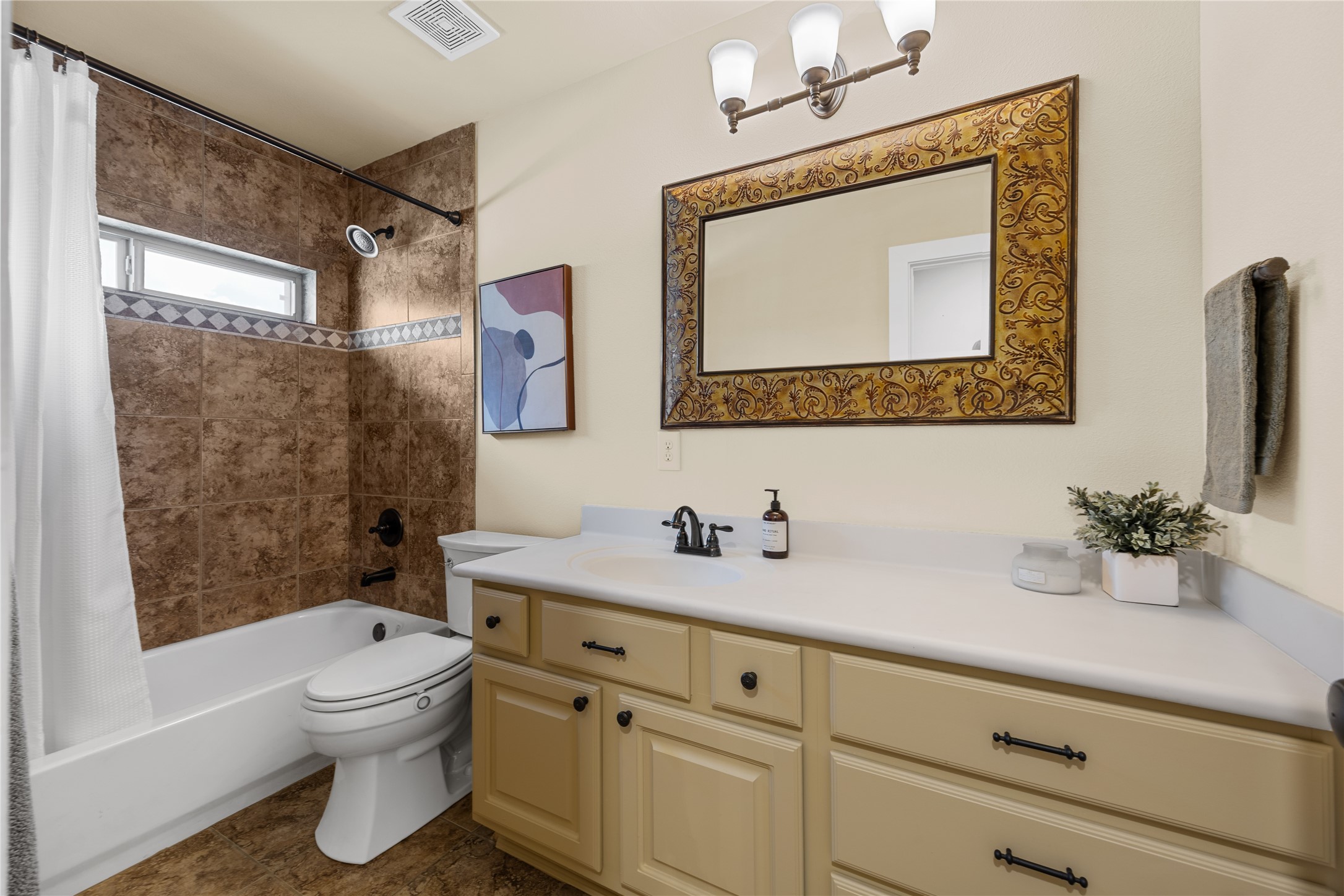 Spacious secondary bathroom featuring a tub/shower combination with decorative tile accents, generous vanity counter space, and cabinet storage.
