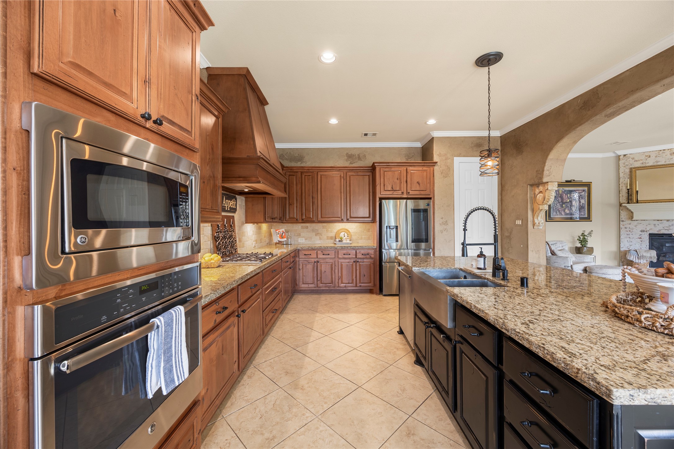Spacious kitchen featuring granite countertops, abundant wood cabinetry, stainless steel appliances, a double-basin farmhouse sink, and an oversized island.