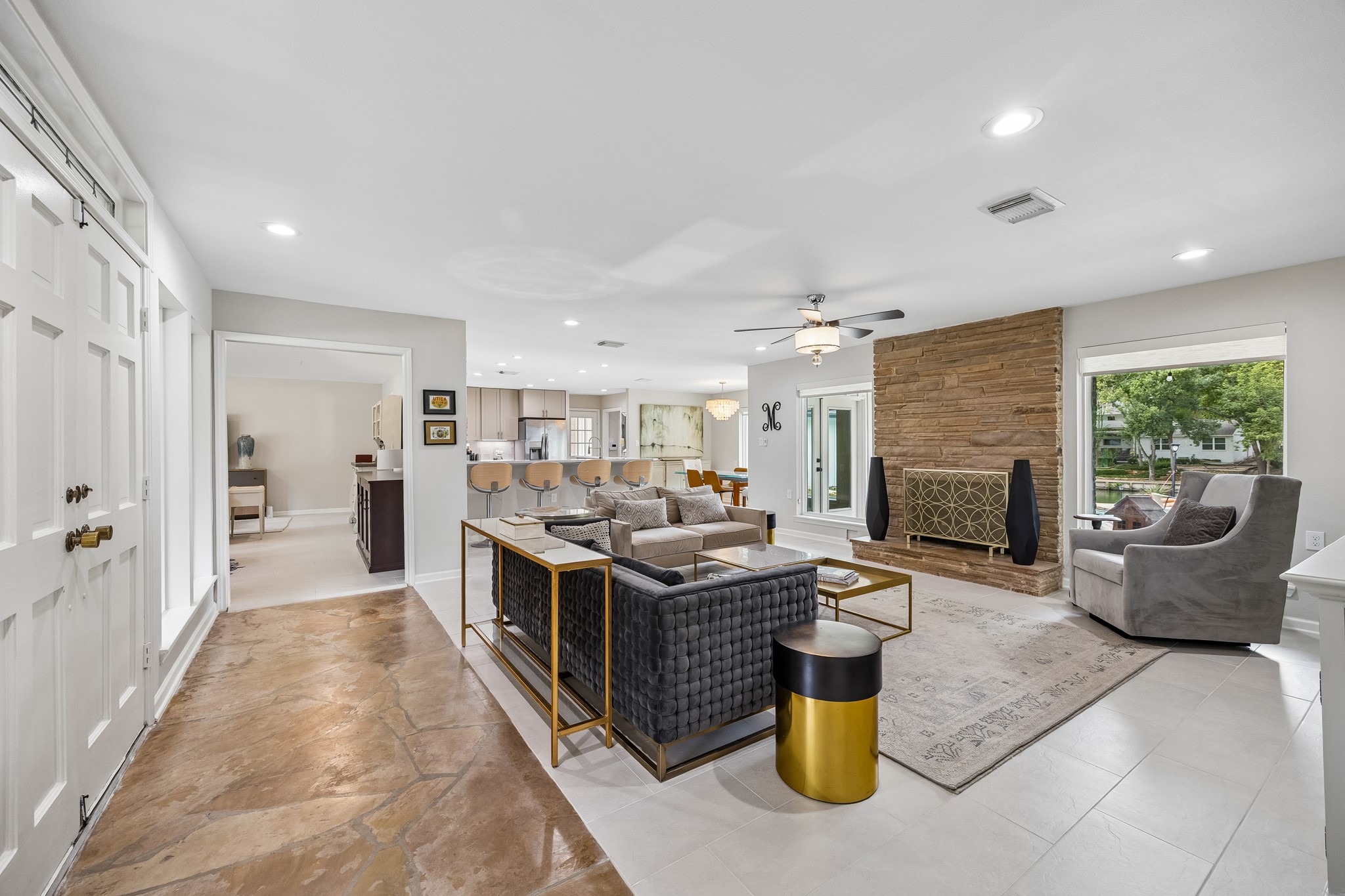 Step through the entry doors into a welcoming living room anchored by a striking original stacked stone fireplace. Original stone floors meet newly tiled flooring that flows throughout the home, while a stylish ceiling fan adds a nice touch. Step through the entry doors into a welcoming living room anchored by a striking original stacked stone fireplace. Original stone floors meet newly tiled flooring that flows throughout the home, while a stylish ceiling fan adds a nice touch.