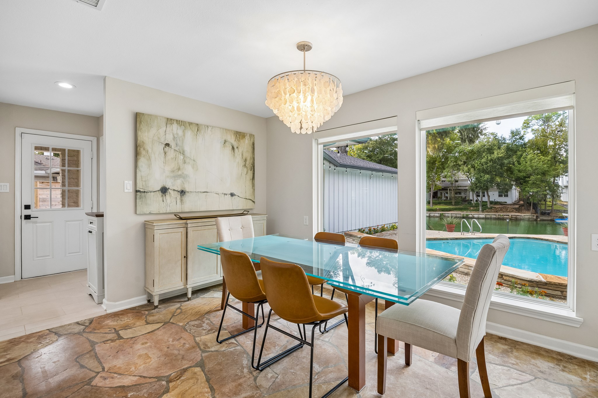 Light-filled eating area featuring original stone flooring, expansive windows overlooking the pool and lake, and a convenient side door providing direct access to he driveway.