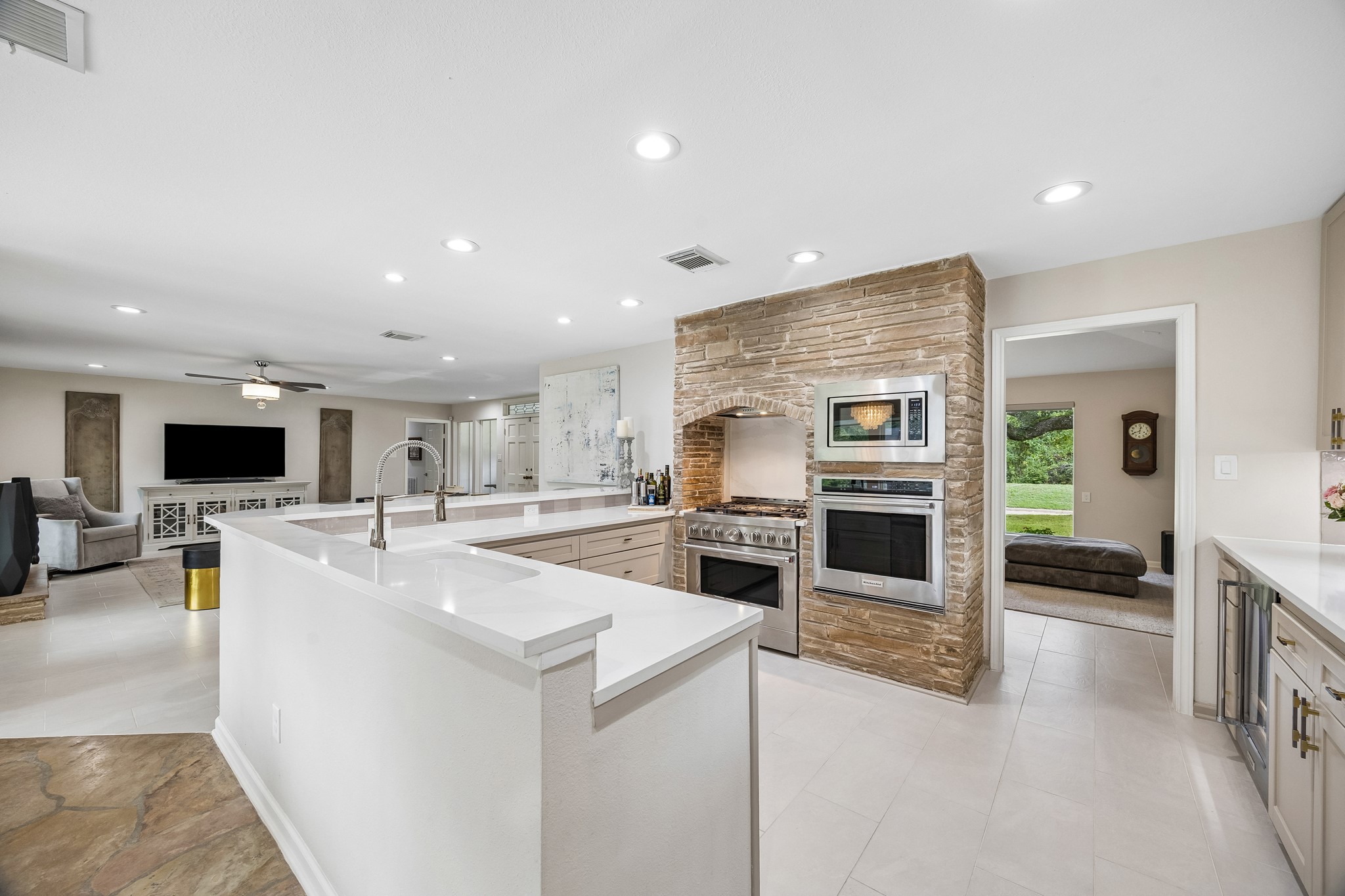 Beautifully appointed kitchen featuring a striking stone-accented wall, a KitchenAid stainless steel appliance suite, with a wall oven, microwave, range with 6-burner gas cooktop, dishwasher, and beverage chiller. A perfect blend of modern elegance and timeless warmth.
