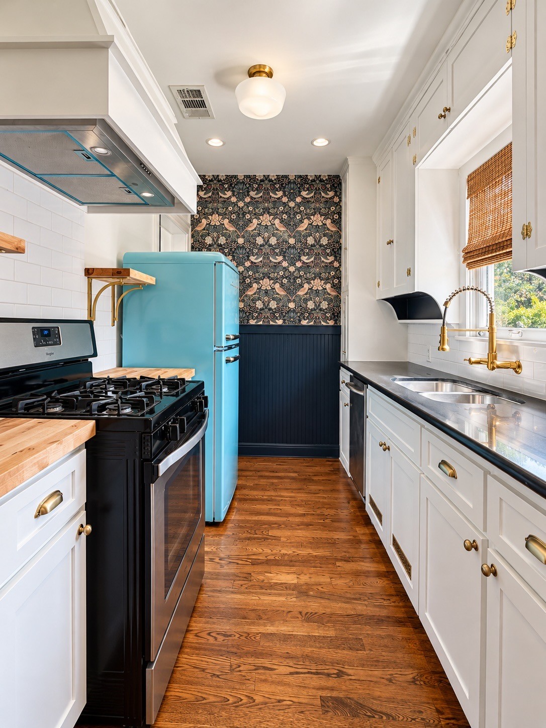 Updated kitchen with retro-inspired turquoise refrigerator, statement wallpaper, brass accents, and beautiful cabinetry.