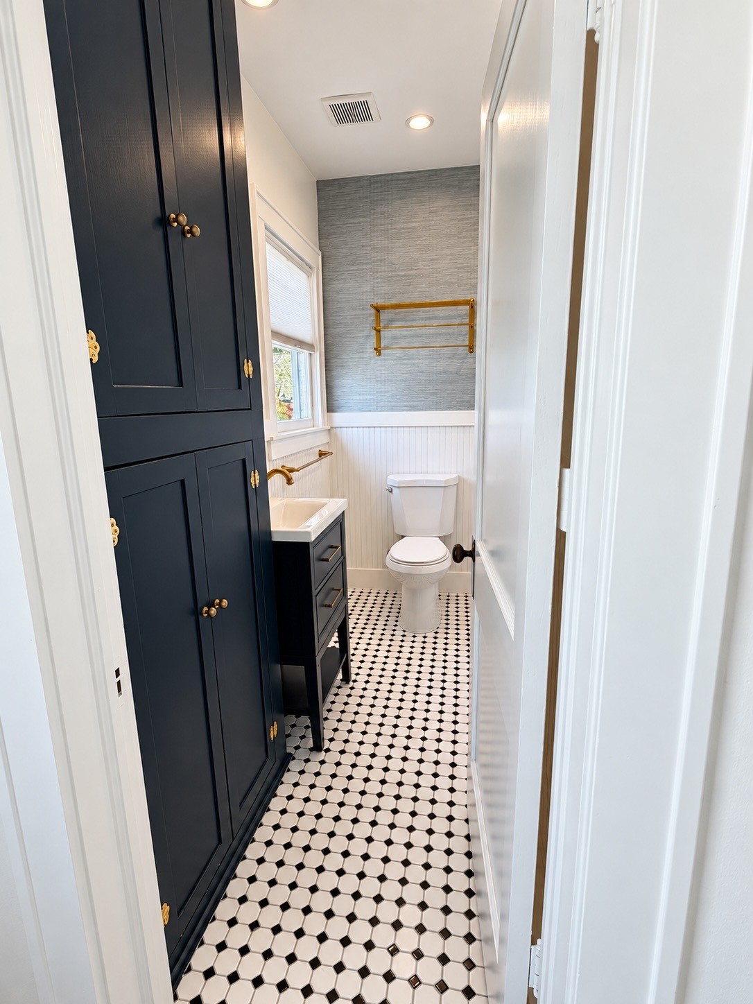 Updated bathroom featuring patterned tile, rich navy cabinetry, brass fixtures, and stylish finishes.