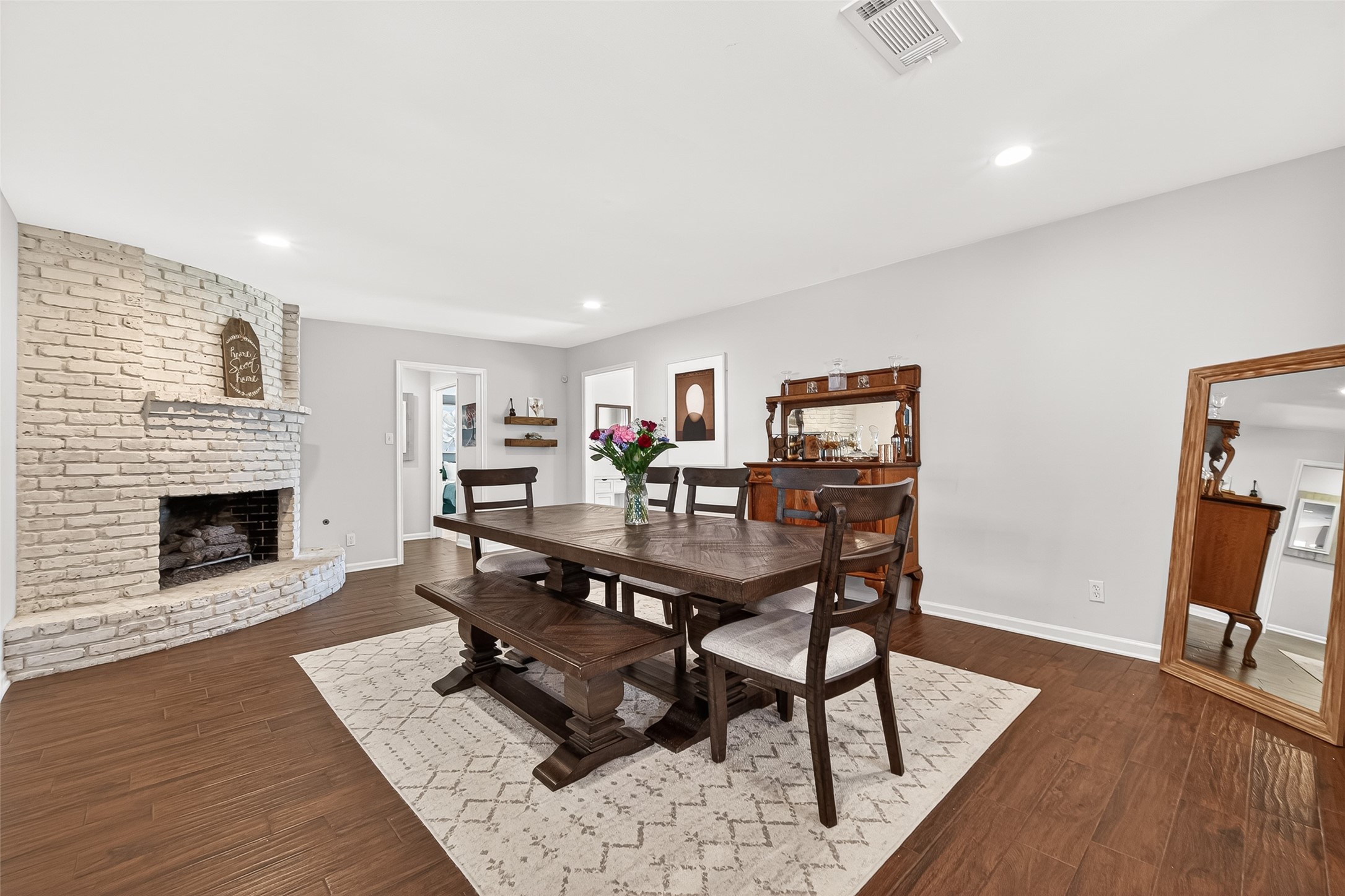 This inviting dining room features a cozy white brick fireplace, and beautiful wood-like tile floors. It offers a warm and welcoming atmosphere, perfect for family gatherings.
