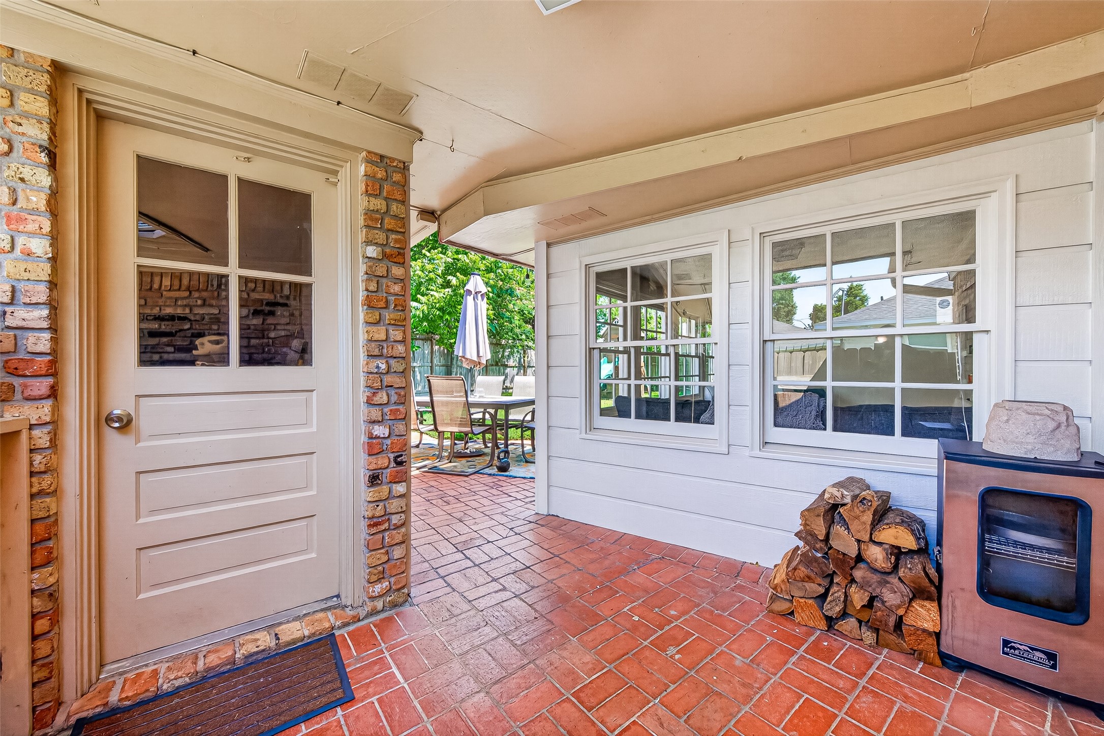 This photo showcases a cozy patio area with brick flooring, a side door, and large windows providing natural light.