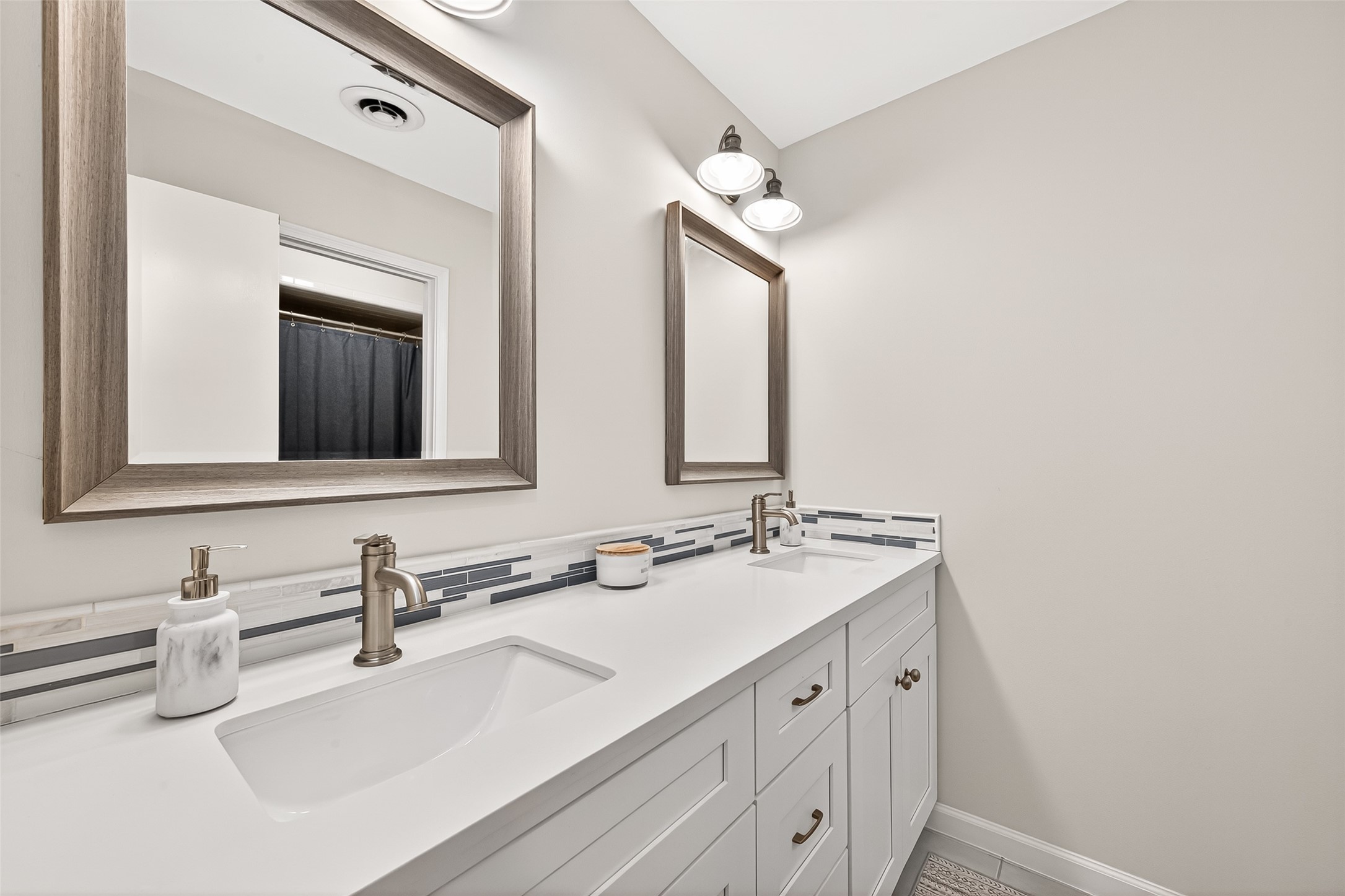 This modern bathroom features dual sinks with sleek fixtures, stylish framed mirrors, and a contemporary backsplash, offering both functionality and elegance.