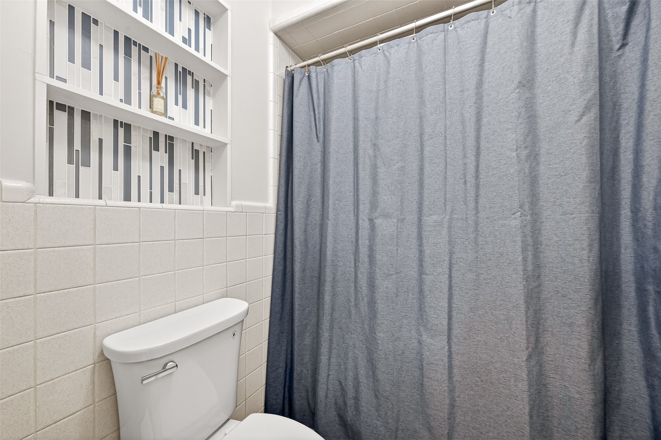 This bathroom features a neatly tiled wall and a shower-tub combination. Built-in shelving provides stylish storage, accented with geometric tile patterns.