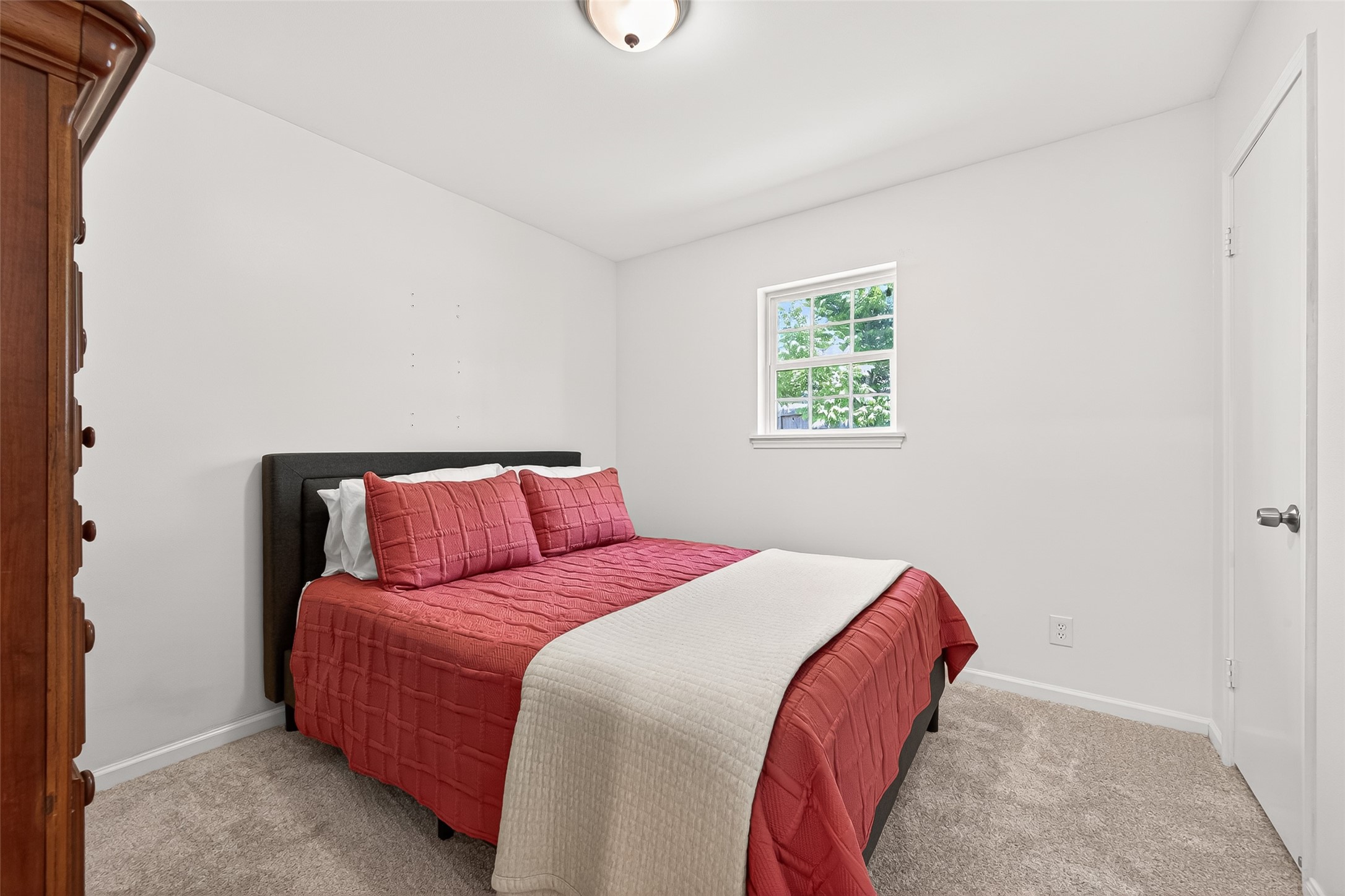 Secondary bedroom with a soft, neutral color palette. A window allows natural light to brighten the space, complemented by carpeted flooring and simple decor.