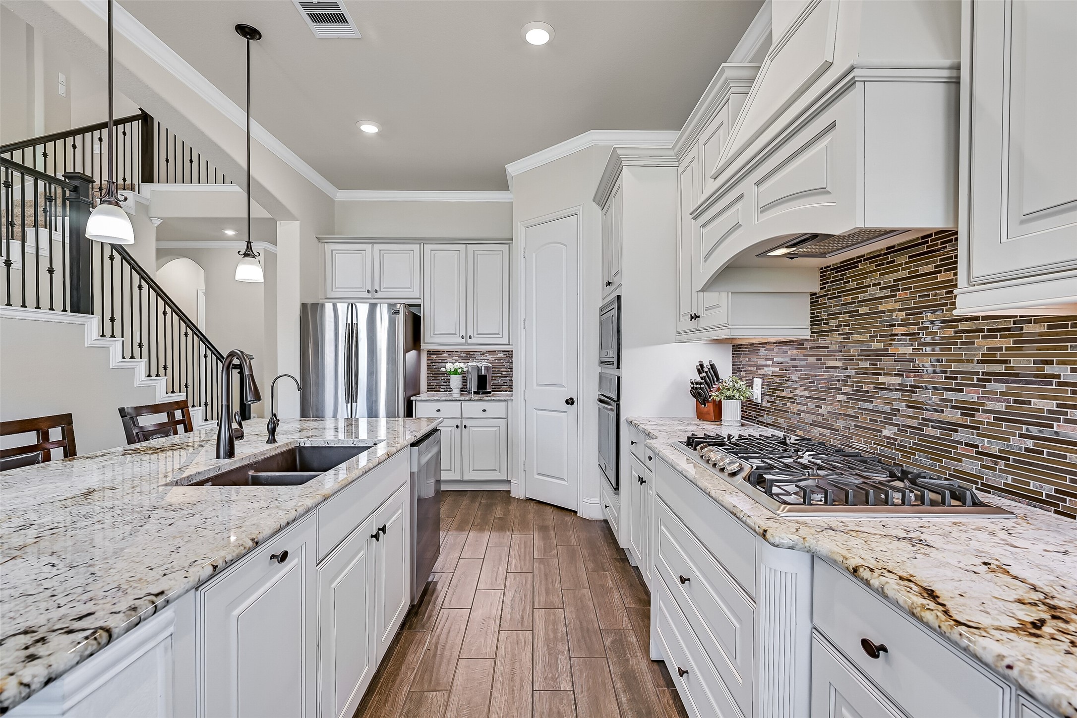 This angle highlights the kitchens well-planned workspace, with generous granite prep surfaces, a dual-basin composite sink with revere osmosis water filtration, a five-burner gas cooktop, built-in oven and microwave, and a corner walk-in pantry. Abundant cabinetry keeps everything organized.