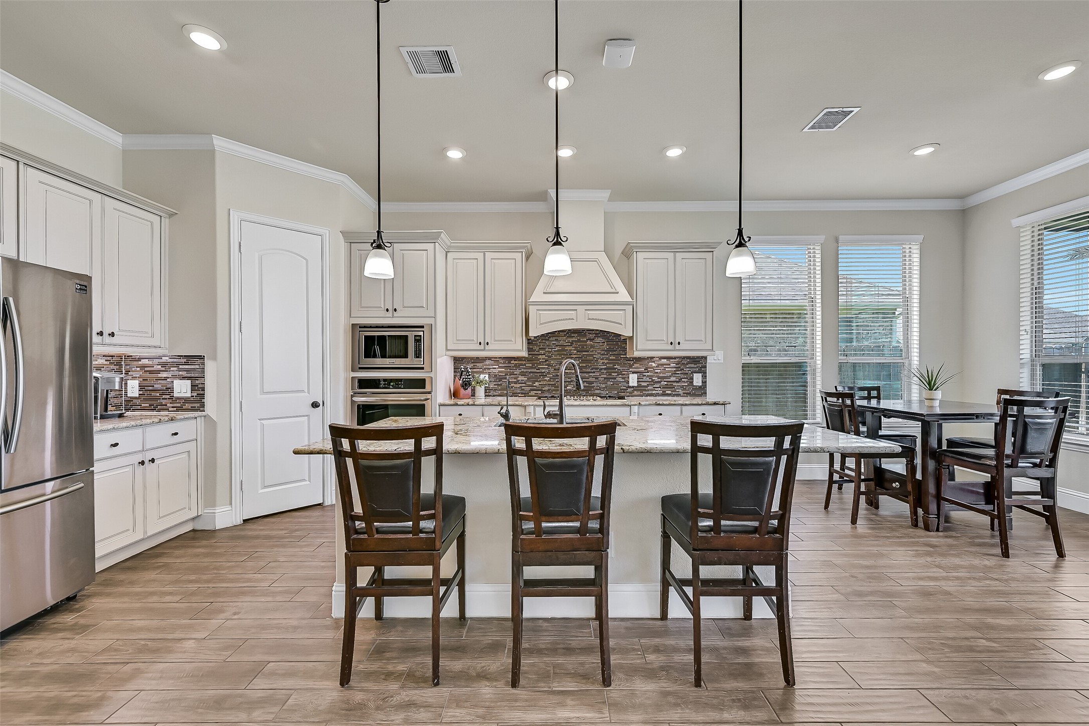 Designed for gathering, this spacious island kitchen offers seating for four, granite countertops, a five-burner gas cooktop, built-in oven and microwave, under-cabinet lighting, abundant cabinetry, and a walk-in corner pantry. The breakfast area overlooks the backyard, making everyday meals feel bright and inviting.
