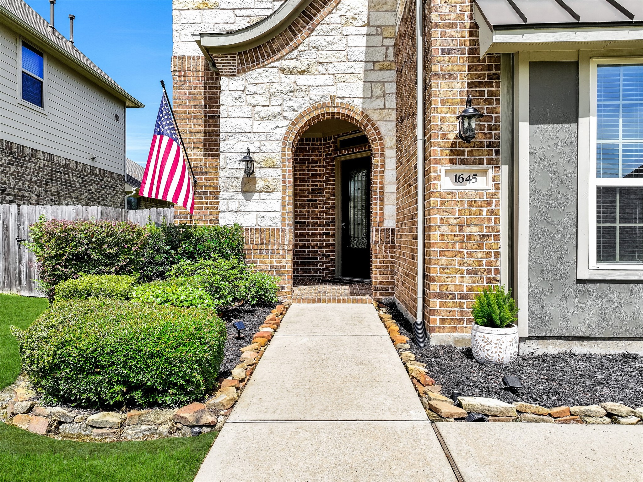 A covered front porch and impressive 8-foot mahogany entry door with pleated glass and wrought iron detailing create a warm welcome for guests. Stone landscape borders, fresh mulch, and mature landscaping enhance the inviting approach to this exceptional home.