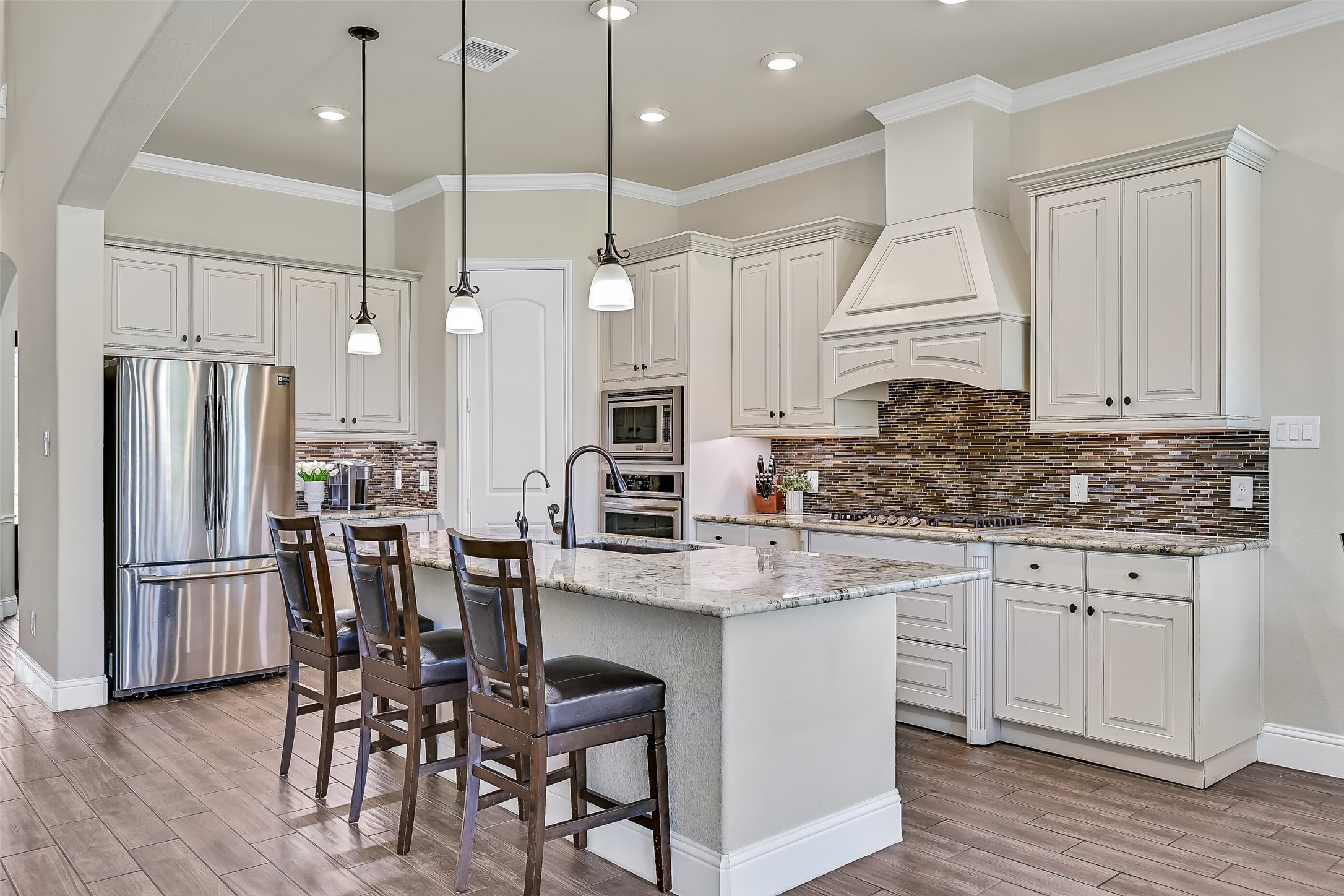 Designed with both style and functionality in mind, the kitchen features granite countertops, a five-burner gas cooktop, built-in oven and microwave, a walk-in corner pantry, and an oversized island with a composite sink, oil-rubbed bronze fixtures, and integrated water filtrationperfect for preparing meals while staying connected to family and guests.