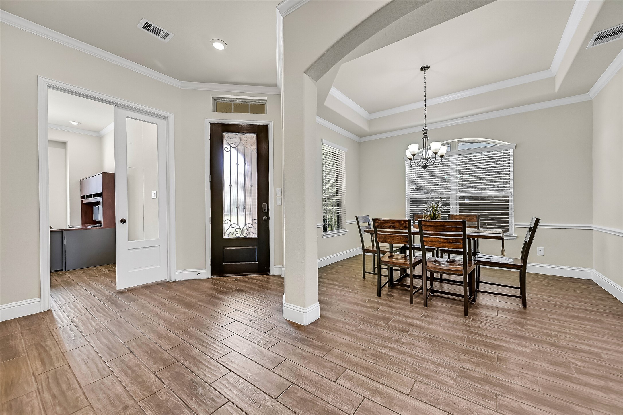 Designed with both beauty and function in mind, the foyer is flanked by a private study with French doors and a formal dining room featuring a tray ceiling, crown molding, and an elegant scrolled iron chandelier. The open layout offers an effortless flow into the heart of the home.