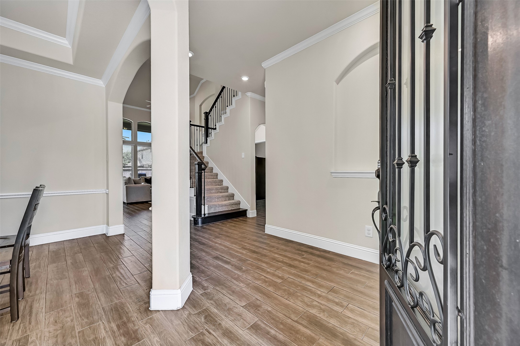 Step inside to soaring ceilings, wood-look tile flooring, extensive crown molding, and elegant architectural details that immediately set the tone. Arched openings, decorative niches, and a split staircase with wrought iron balusters create a grand yet welcoming first impression.