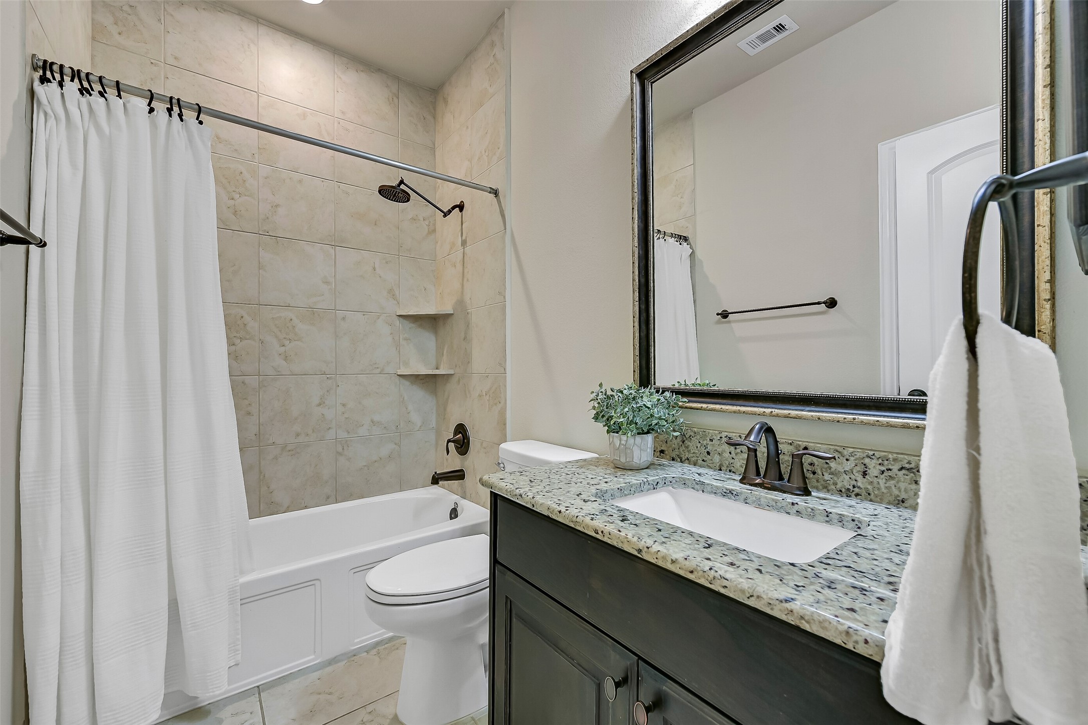 Conveniently located adjacent to the game room and nearby bedroom, this full bath features a granite vanity with a rectangular undermount sink, framed mirror, stained wood cabinetry, and a tub/shower with a tile surroundperfect for everyday use or accommodating overnight guests.