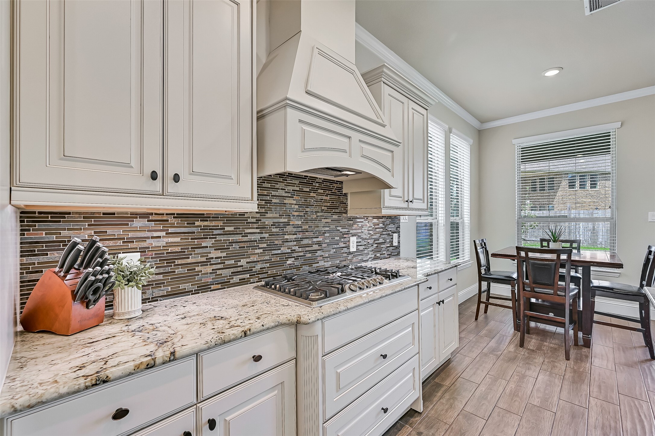 A beautiful glass and stone mosaic backsplash complements the custom vent hood, while extensive cabinetry, generous prep space, and an open layout make this kitchen equally suited for weeknight dinners and holiday gatherings.