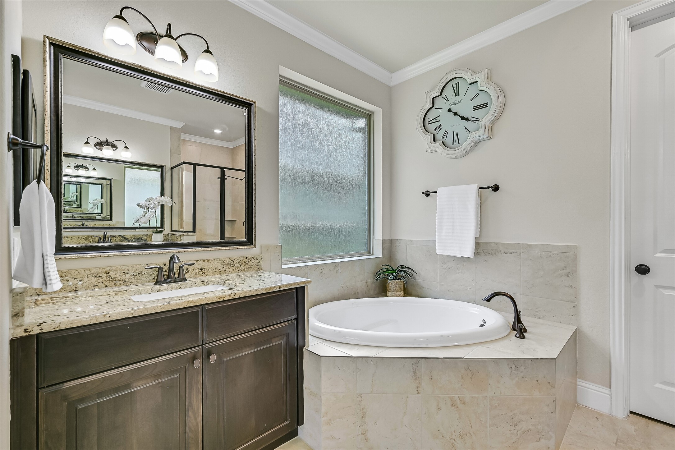 A corner soaking tub beneath the frosted window creates the perfect place to unwind, while the thoughtful layout offers plenty of space to spread out during busy mornings. Every detail balances everyday functionality with a touch of luxury.